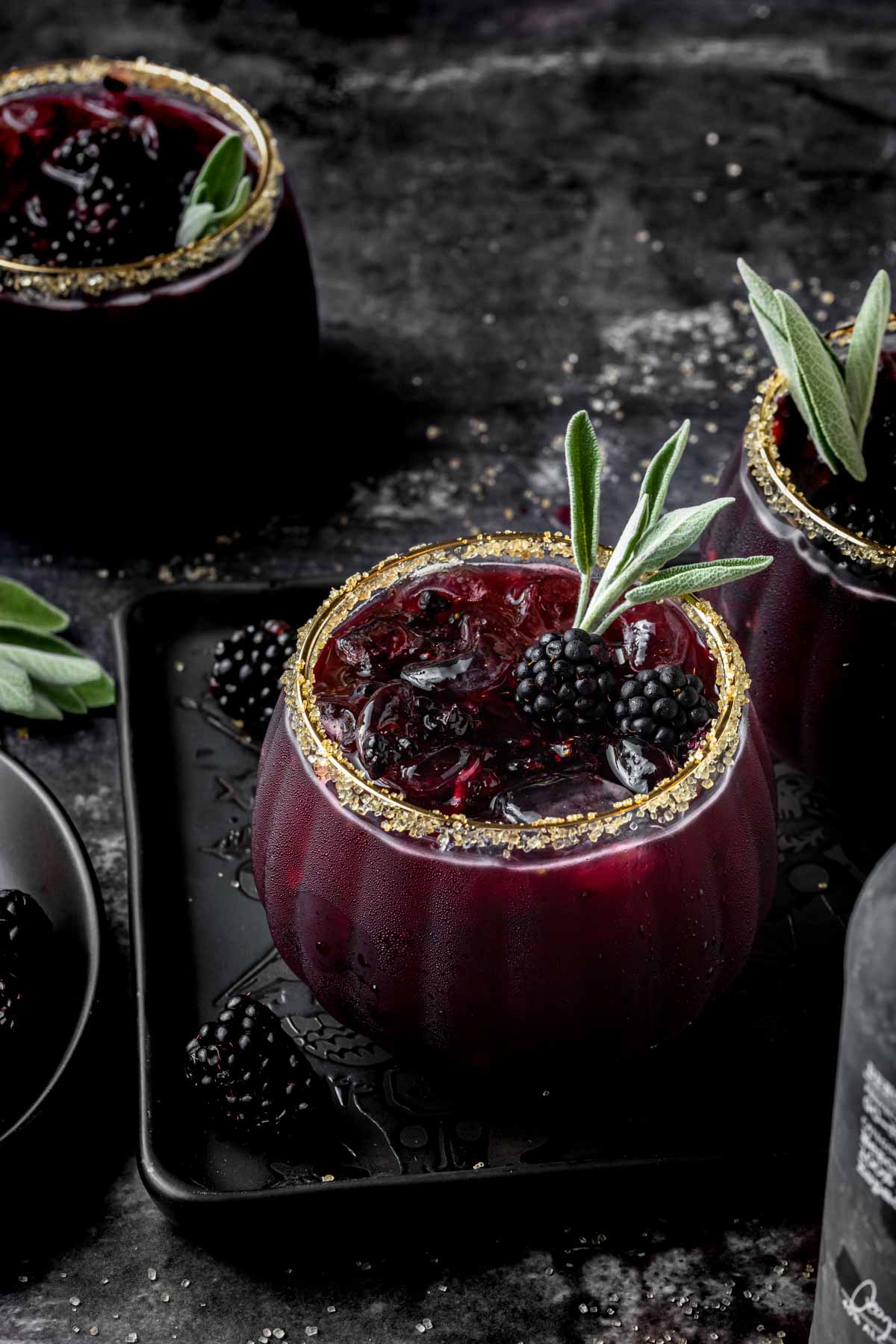 Blackberry margaritas in glasses rimmed with sugar and garnished with sage. 