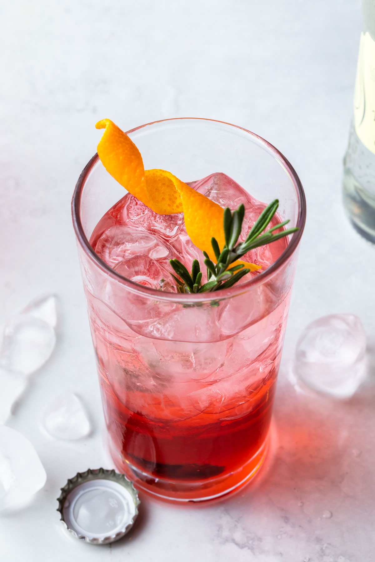 Campari tonic in a high ball glass garnished with a fresh rosemary sprig and a twist of orange. 