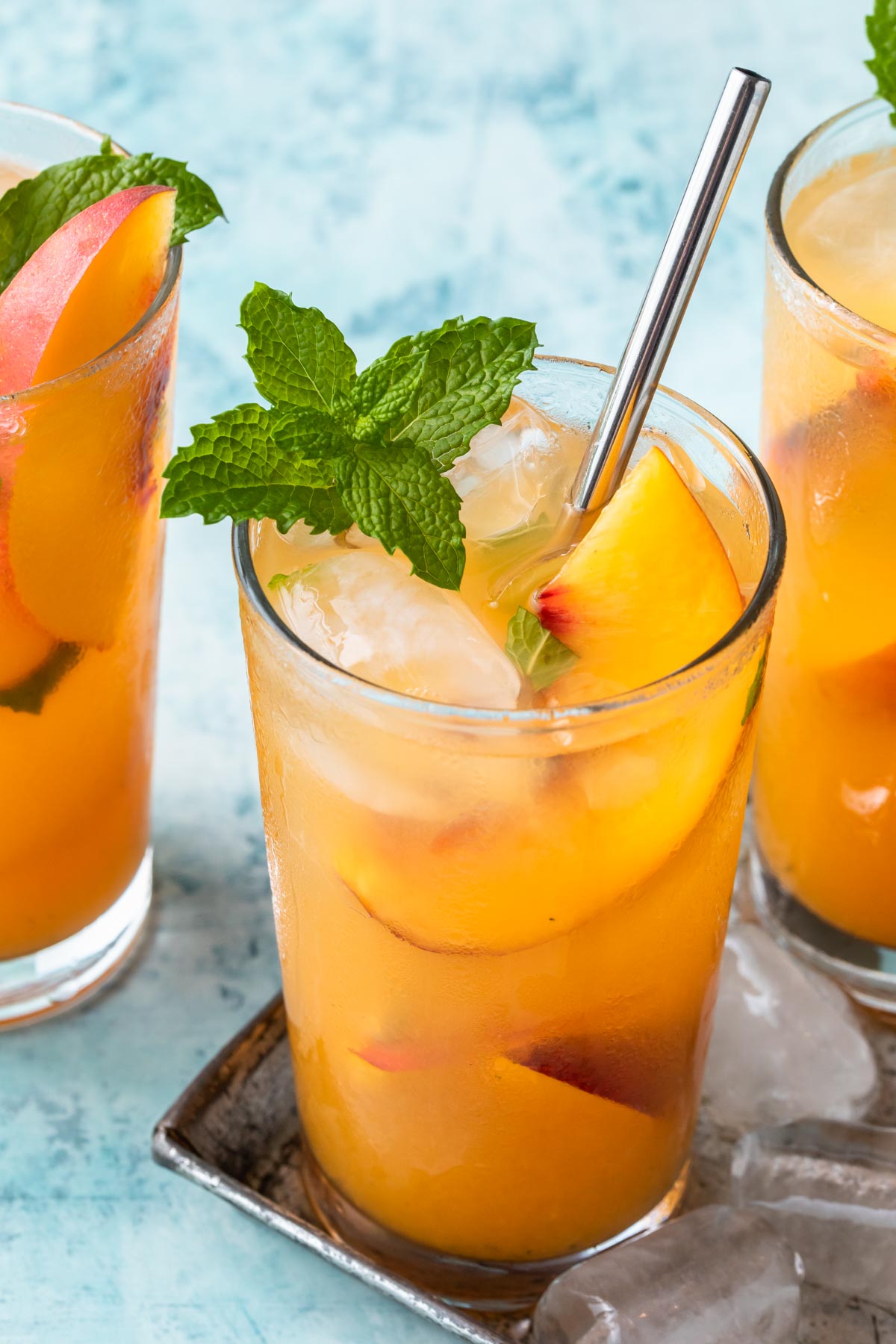 Peach mojito in a tall glass with a metal straw, mint leaves and a peach slice for garnish.