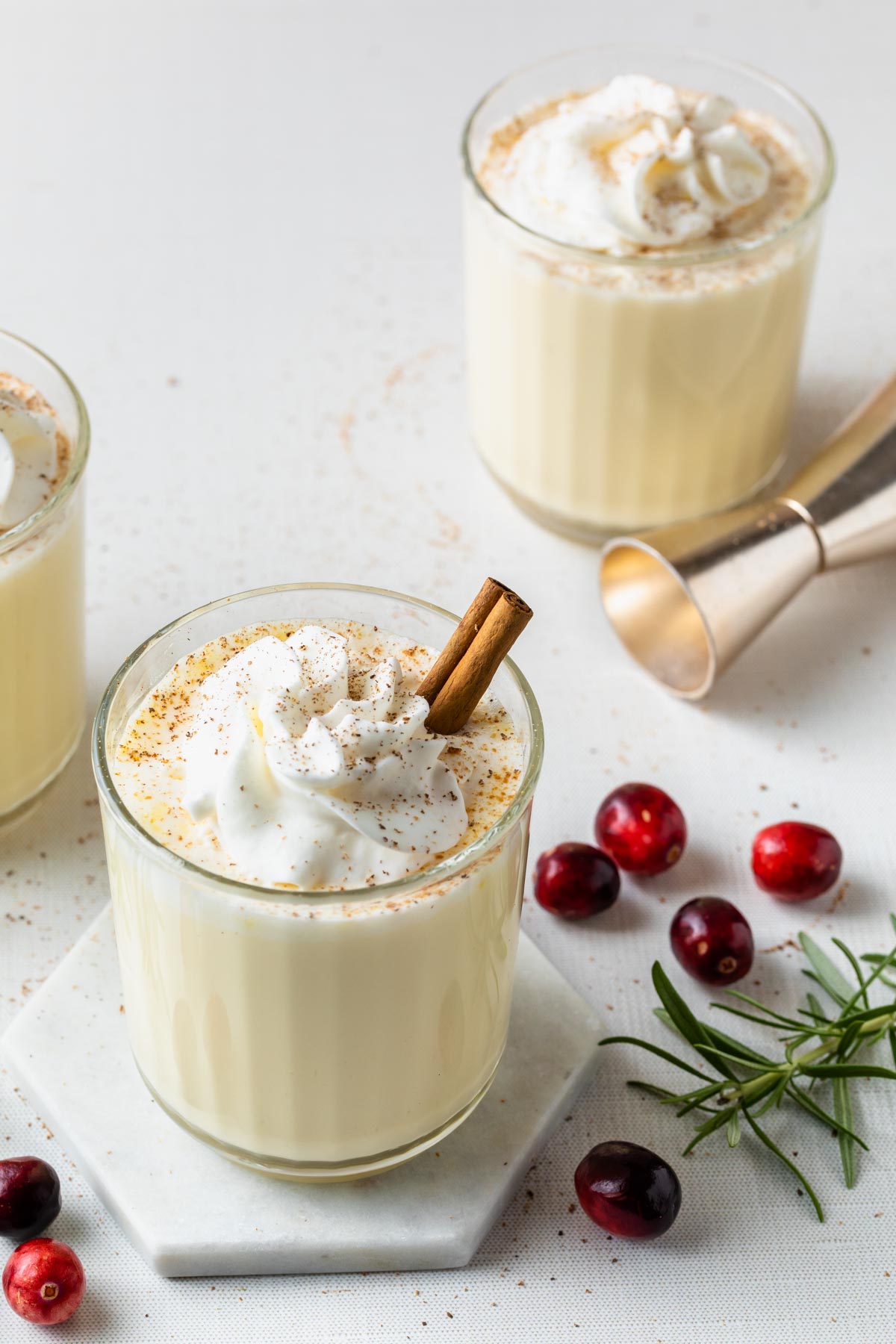 An old fashioned glass of eggnog topped with whipped cream, sprinkled with nutmeg and garnished with a cinnamon stick. 