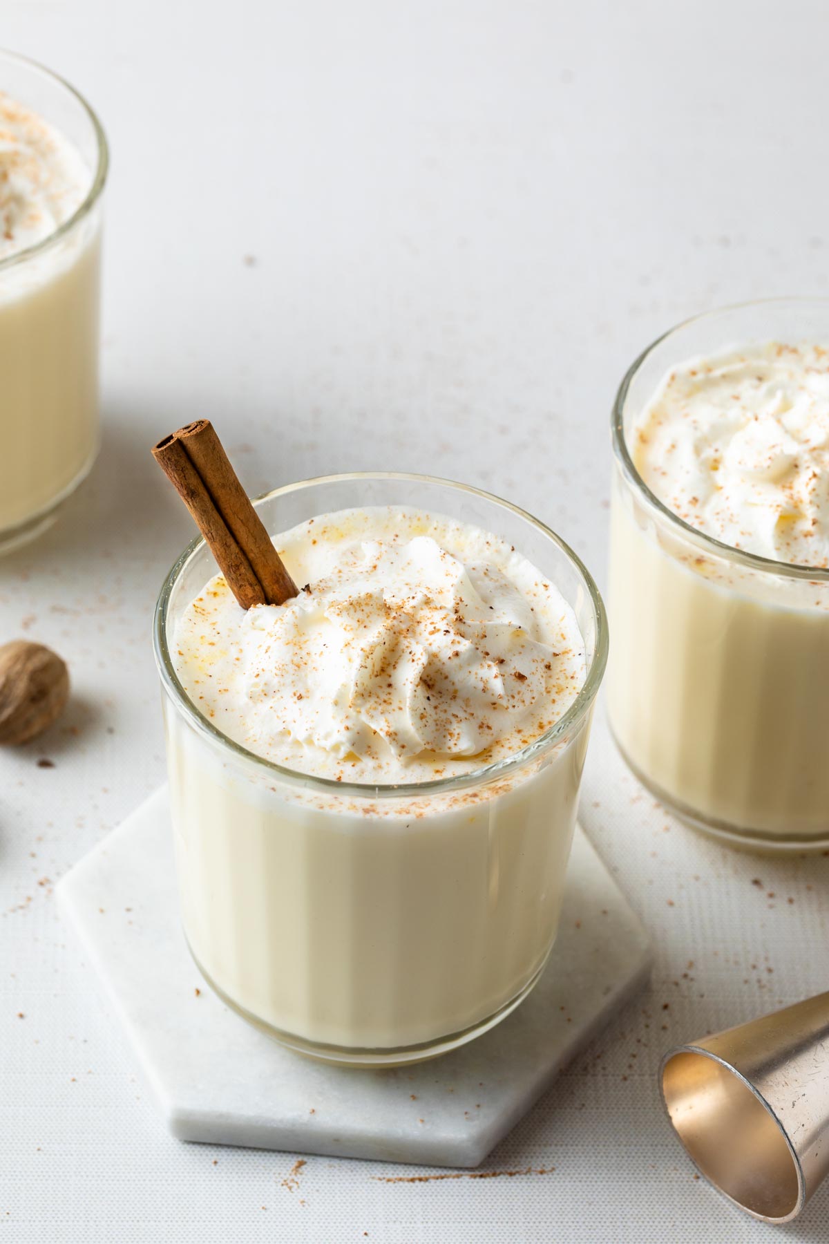 Eggnog in a old fashioned glass topped with whipped cream and sprinkled with nutmeg and garnished with a cinnamon stick.