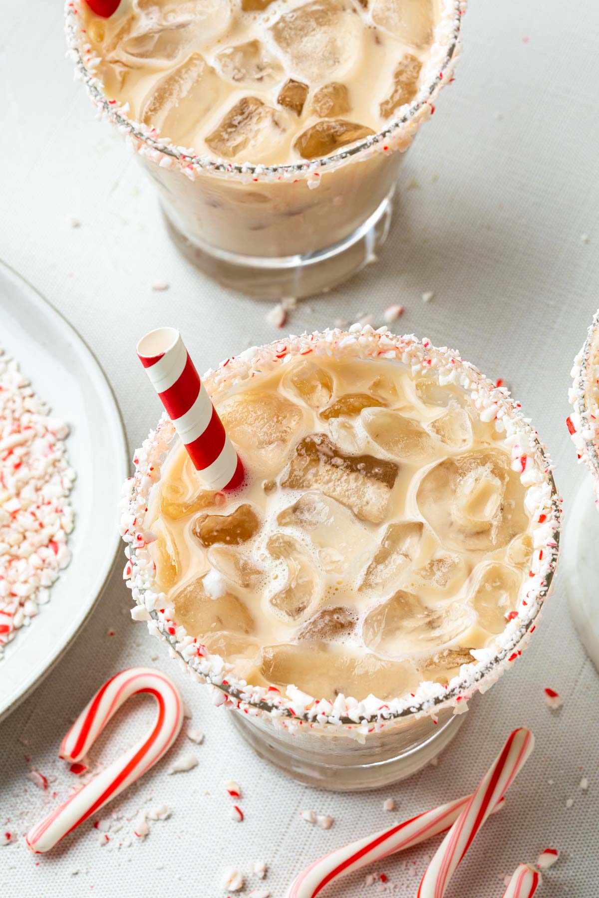 Overhead shot of peppermint cocktails in glasses rimmed with candy cane pieces, with red and white paper straws in the glass. 