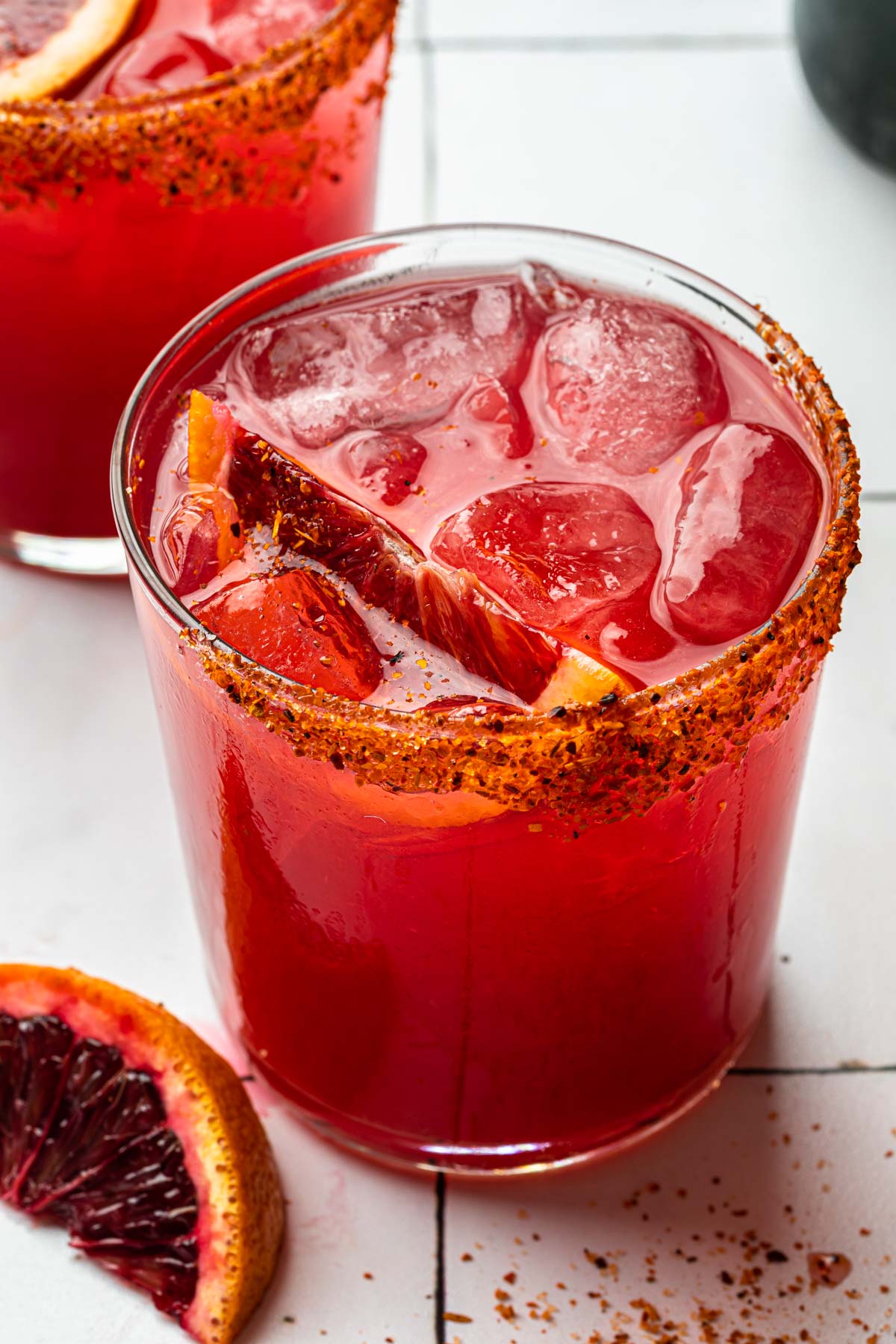 Close up shot of blood orange margaritas in old fashioned glasses rimmed with tajin and garnished with a blood orange wedge.