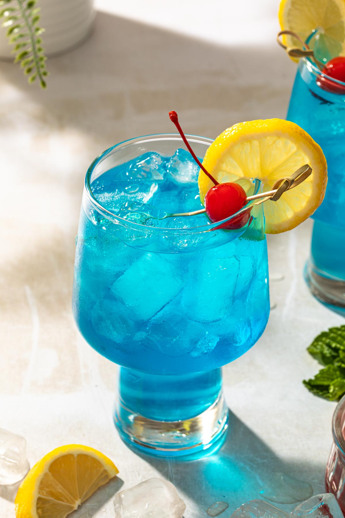 A blue motorcycle cocktail in a glass garnished with a lemon wheel and a cherry. 