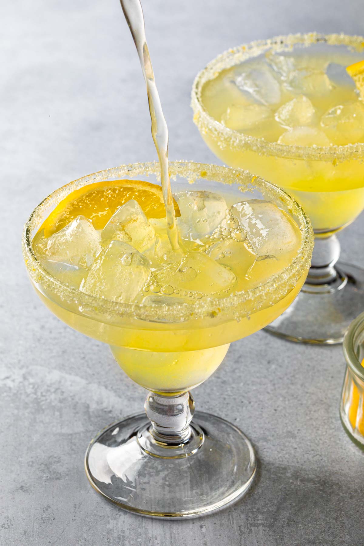 Two limoncello margaritas in glasses, one is being poured. 
