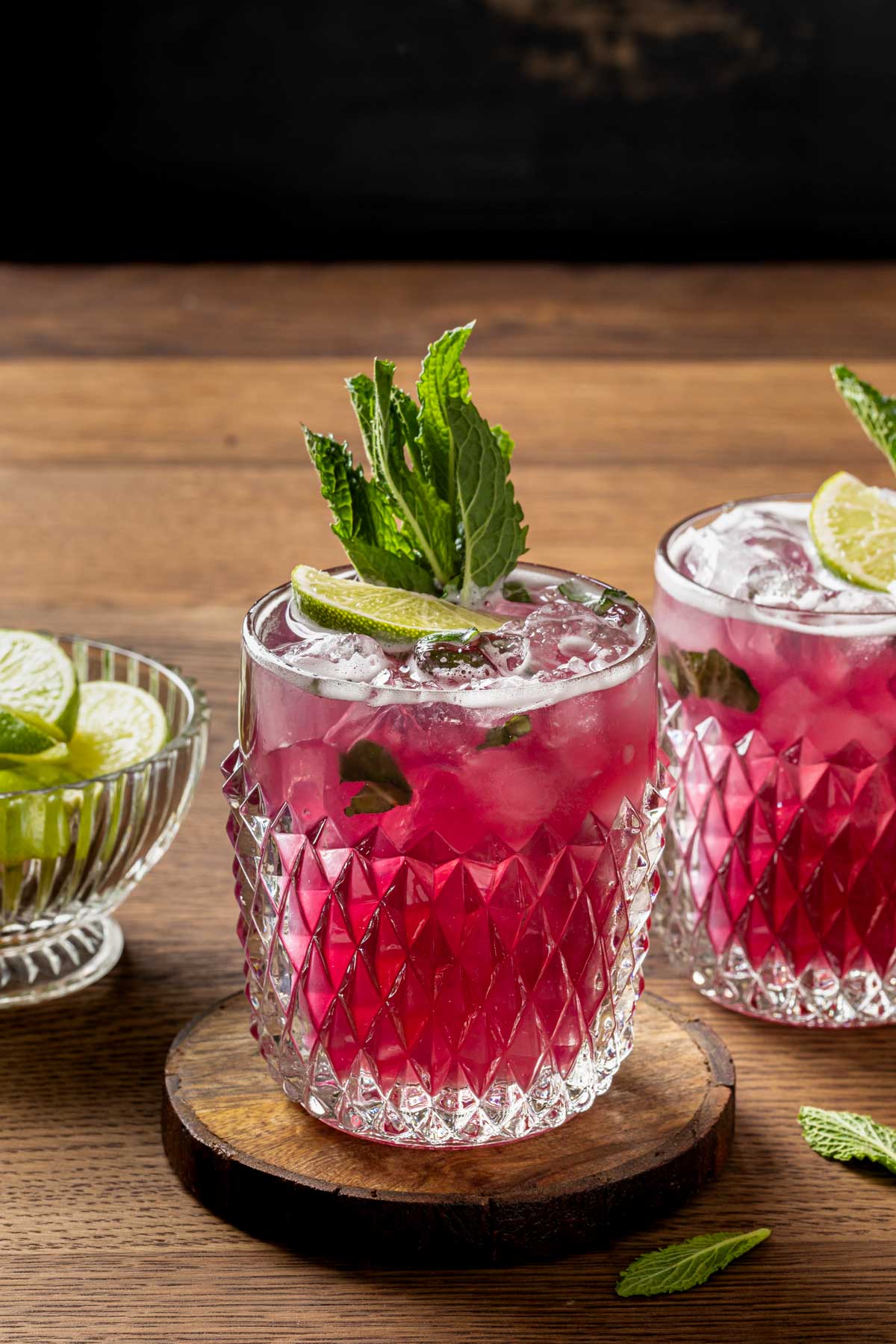 Hibiscus pineapple bourbon cocktails in glasses garnished with mint leaves and lime wedges. 