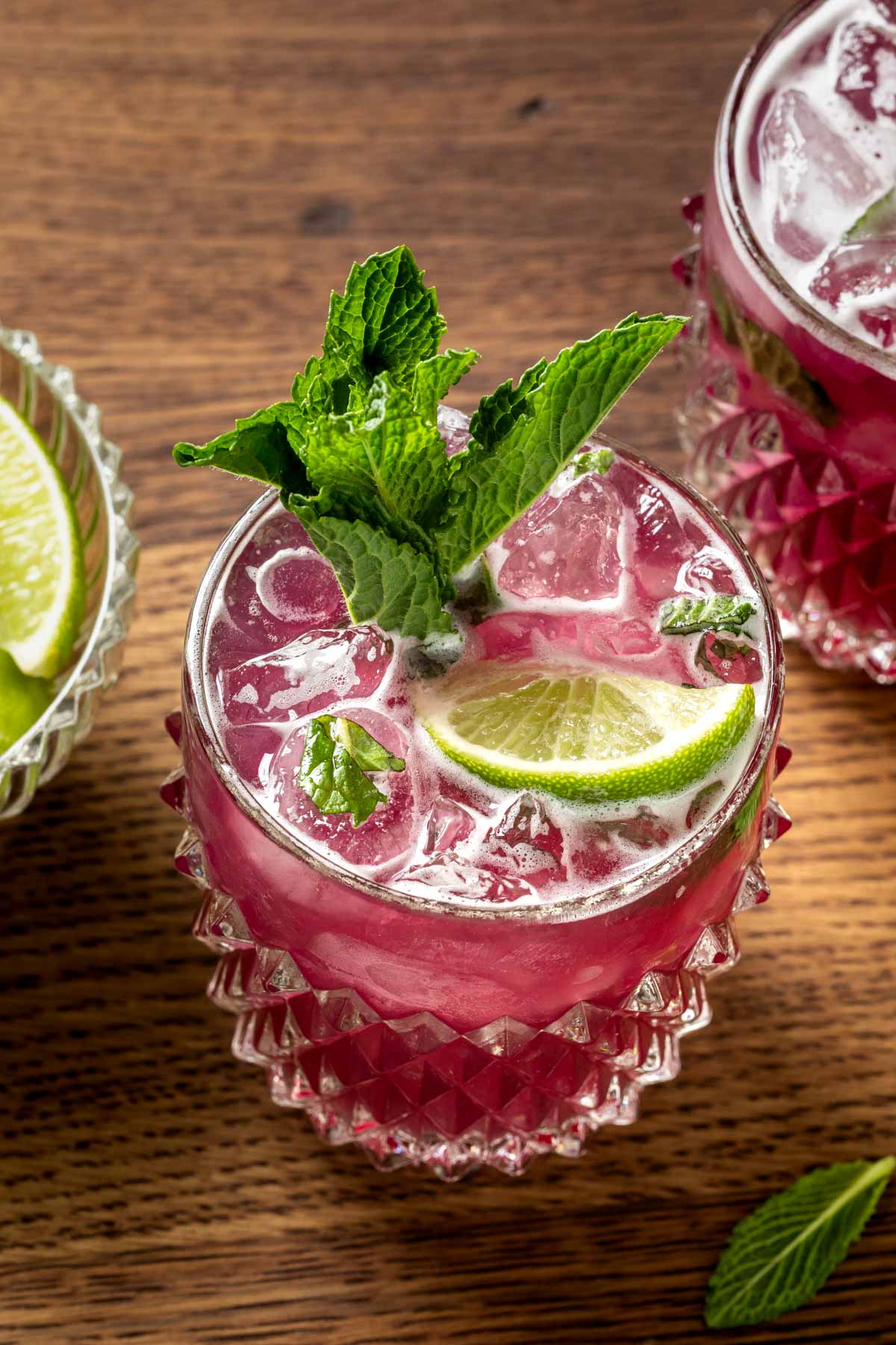 Hibiscus pineapple bourbon cocktails in glasses garnished with mint leaves and lime wedges. 