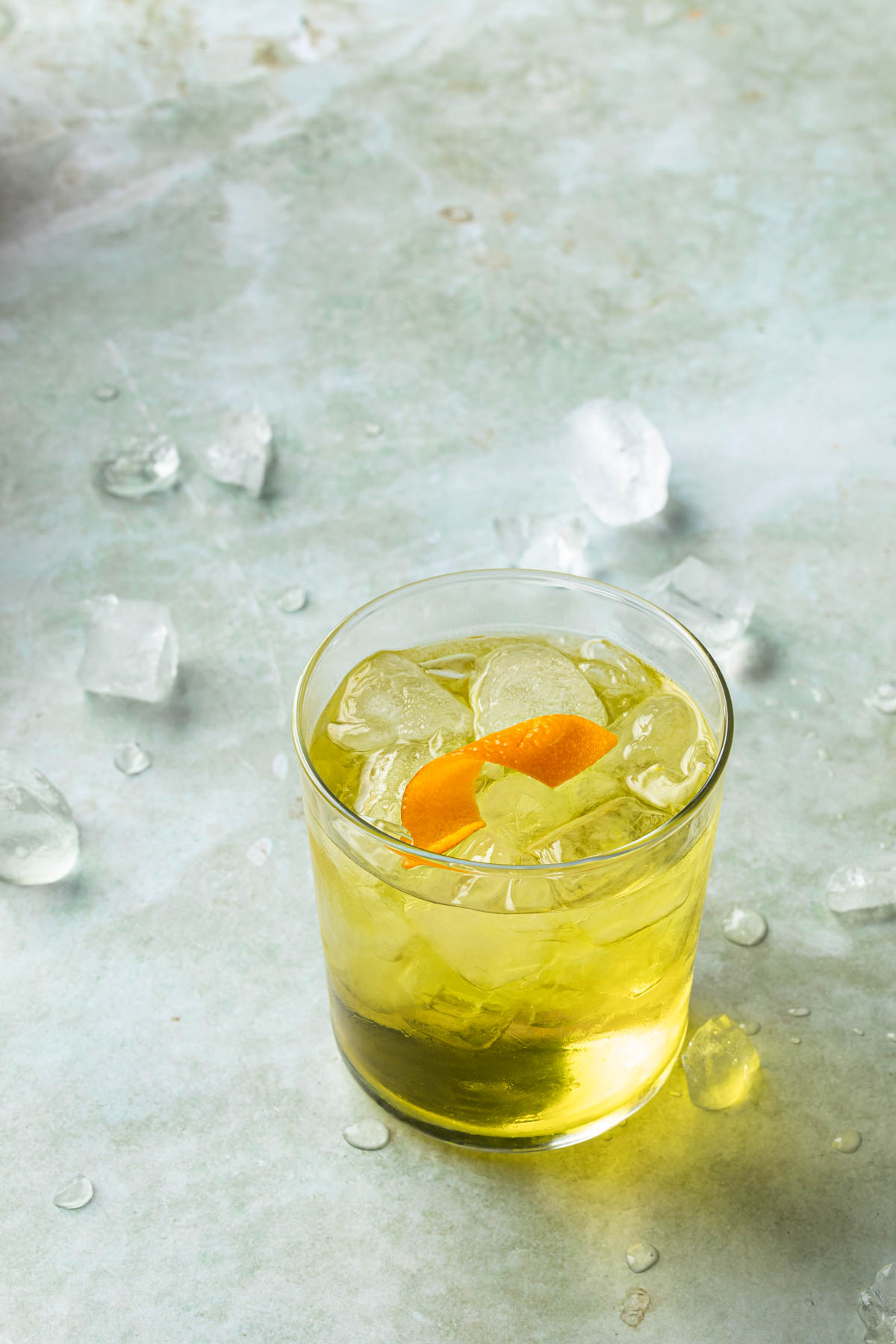 A white negroni in a rocks glass with an orange twist. 