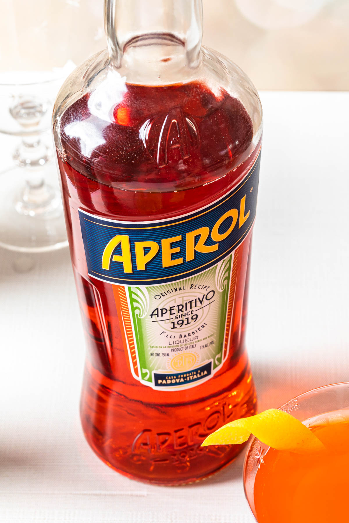 A close up of a bottle of aperol with a cocktail next to it. 