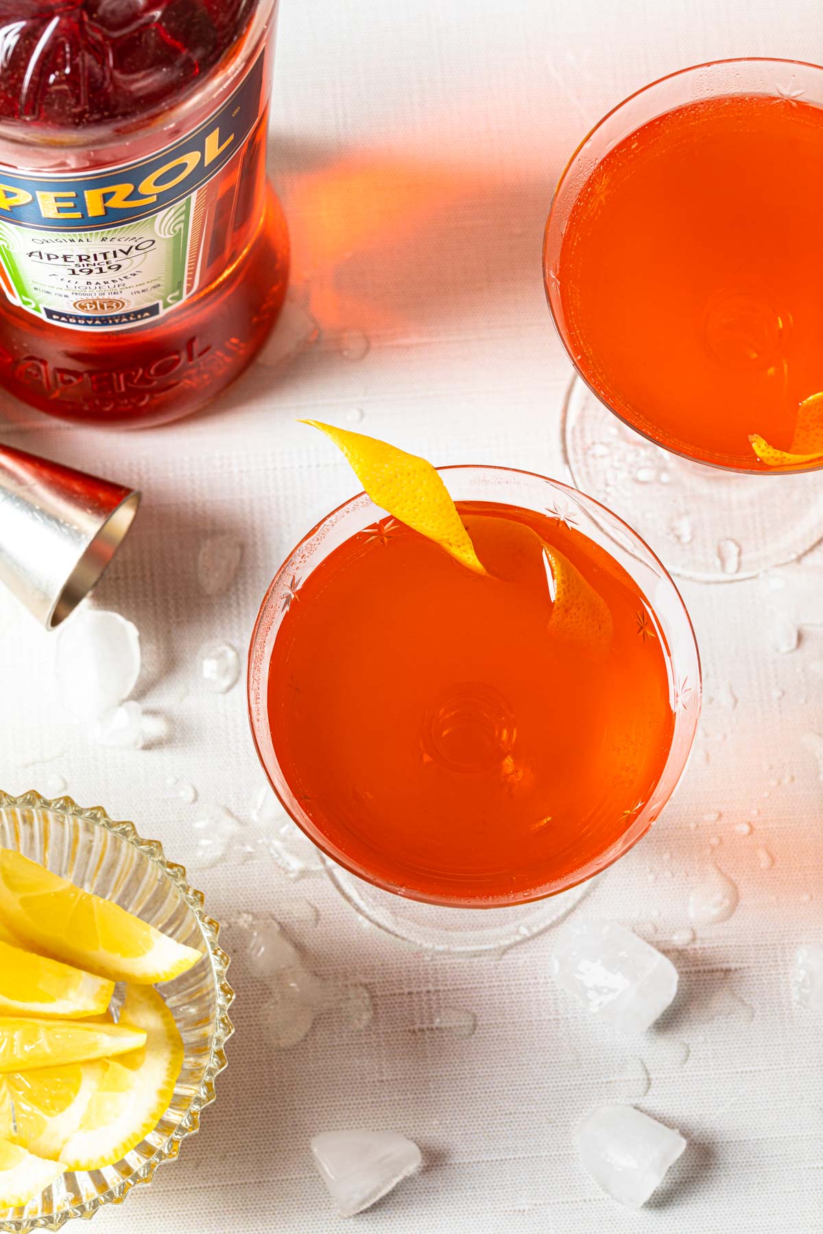 An overhead shot of 2 aperol sours in coupe glasses with lemon twists. 