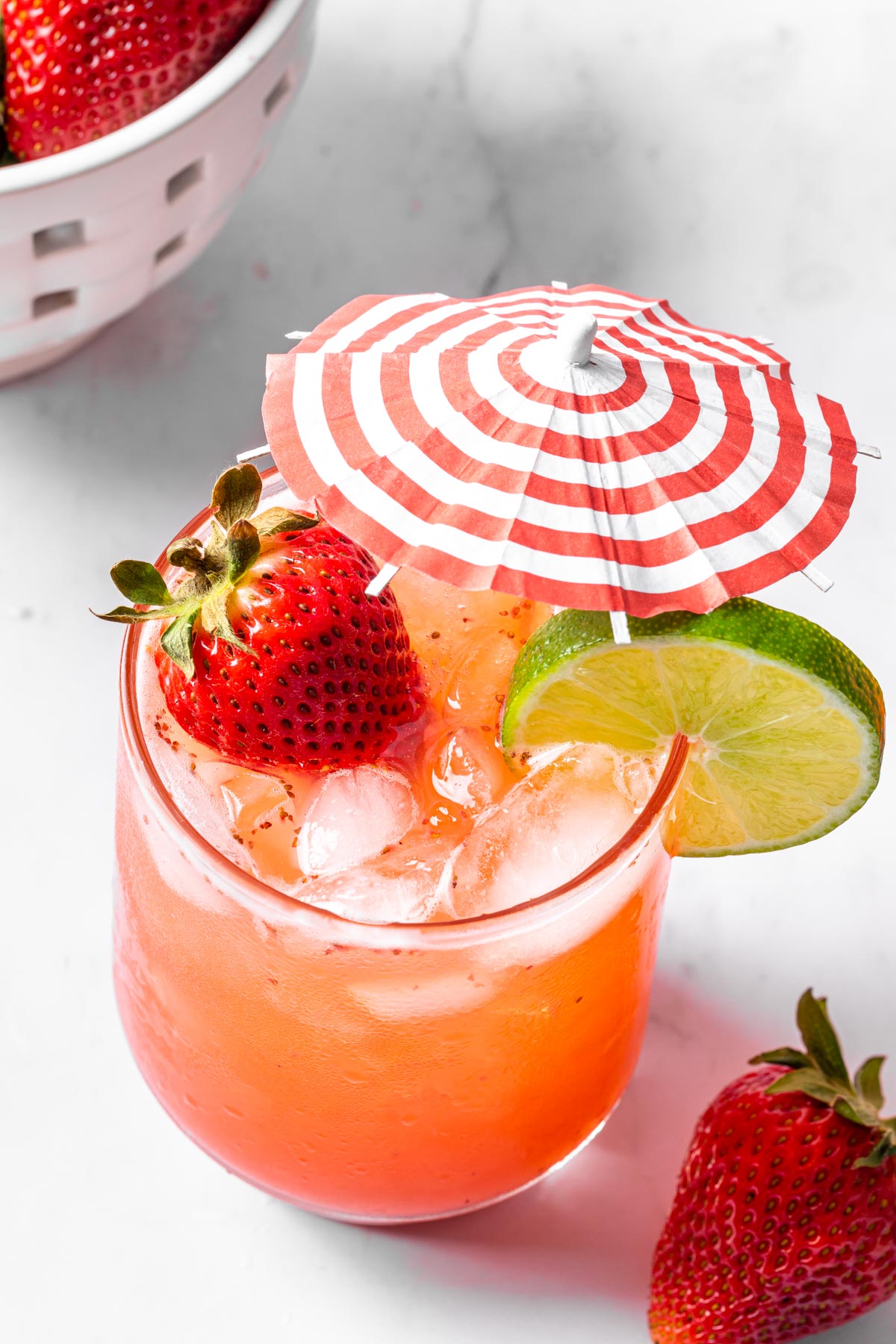 A strawberry mocktail mule with a strawberry and lime wheel for garnish, decorated with a red and white striped cocktail umbrella. 
