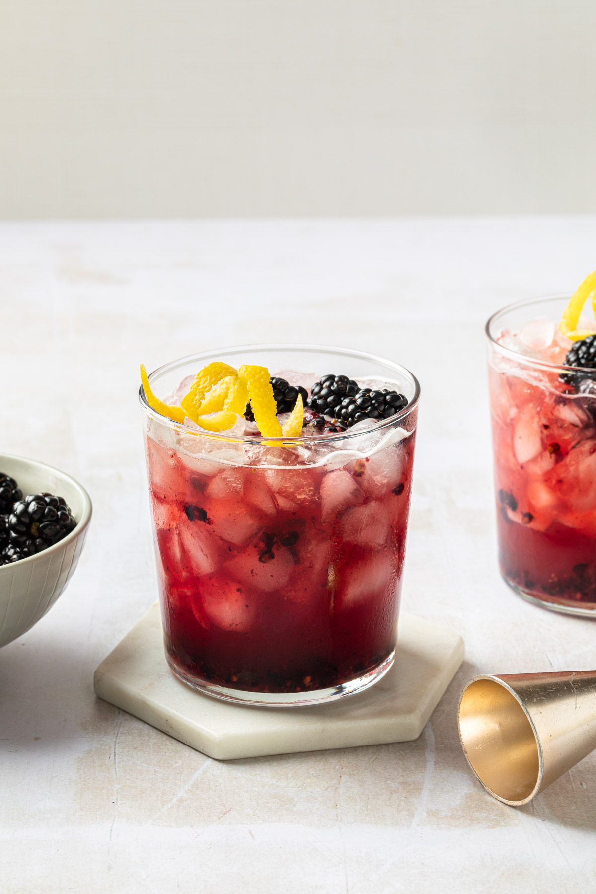 Blackberry bramble cocktails on ice, garnished with blackberries and a lemon twist.