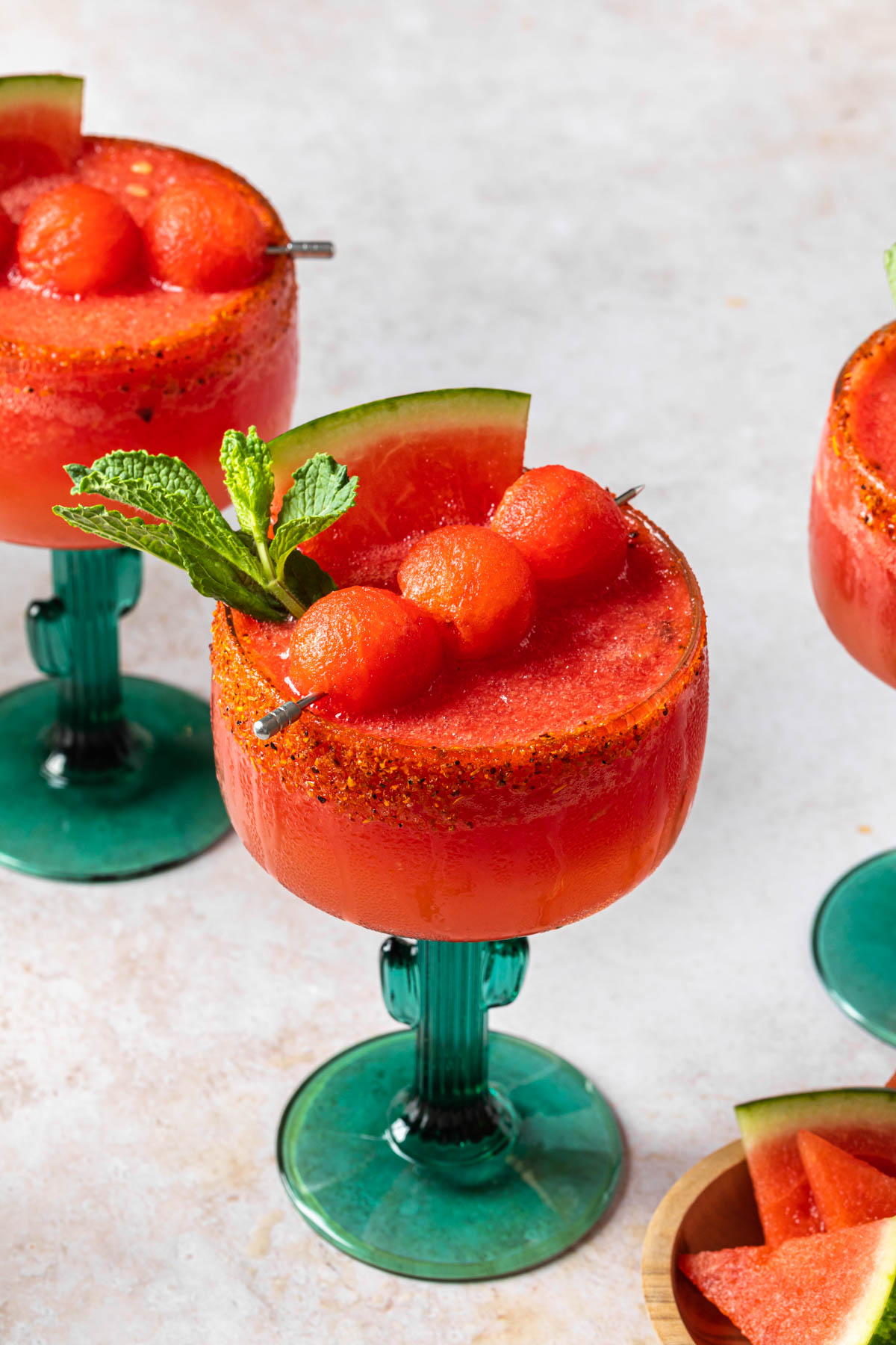 Watermelon margaritas garnished with a watermelon wedges and mint leaves, rimmed with tajin. 