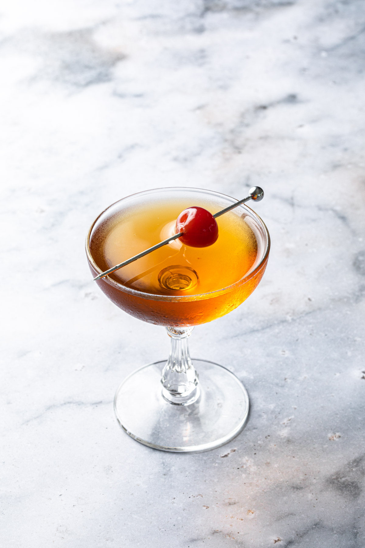 A brandy manhattan in a coupe glass, garnished with a maraschino cherry. 