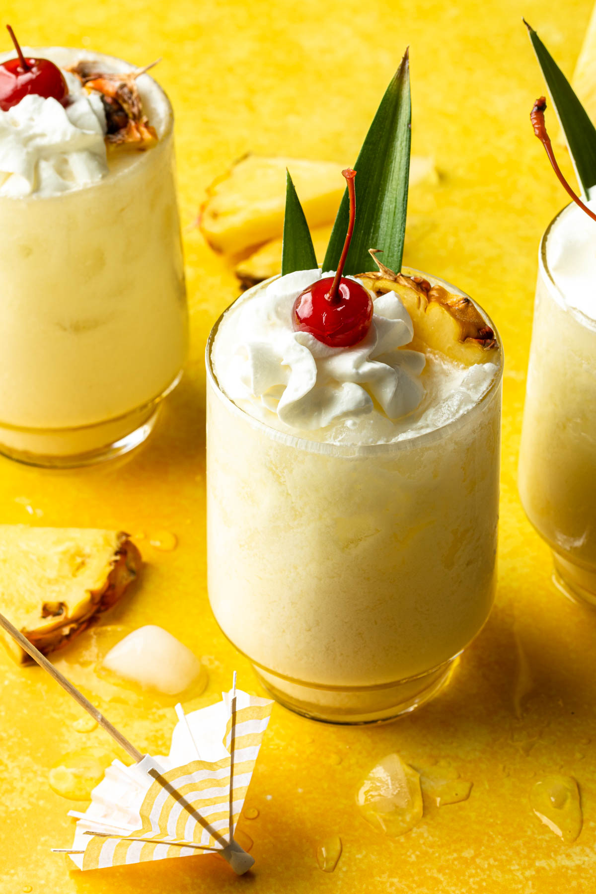 3 pina coladas on the rocks, in glasses garnished with a pineapple wedge, whipped cream and a cherry. 