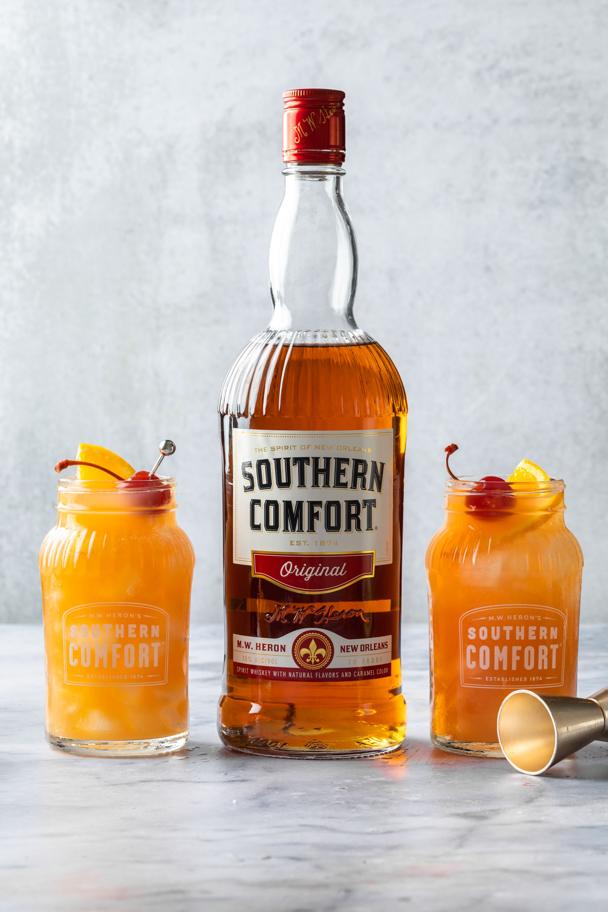 Two southern comfort cocktails in mason jar glasses, with a bottle of southern comfort in between them. 