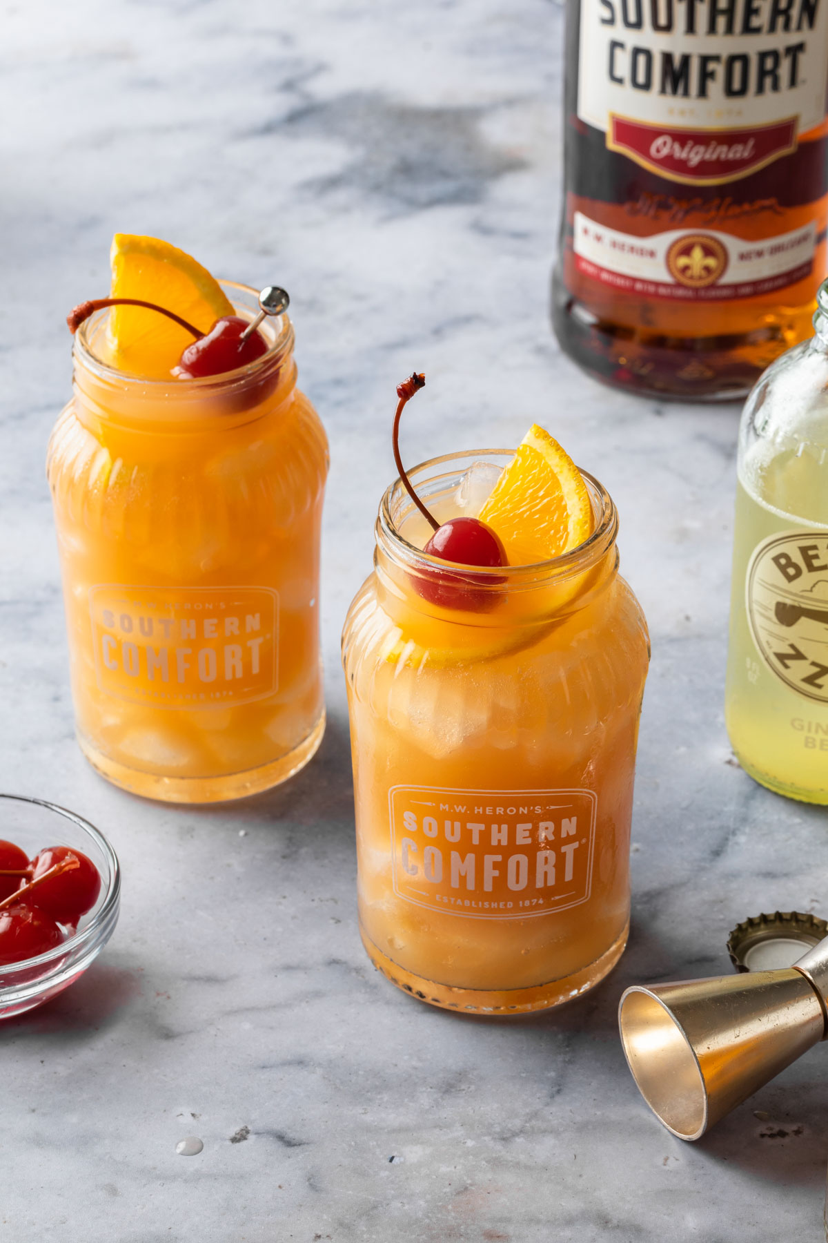 Southern comfort cocktails in mason jar glasses, garnished with orange and cherry. 