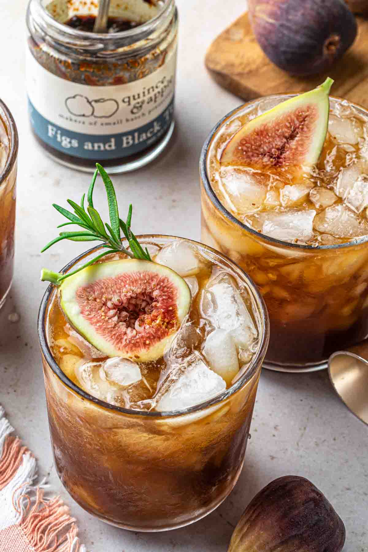 A fig jam whiskey cocktail, garnished with a fig and a sprig of rosemary. 