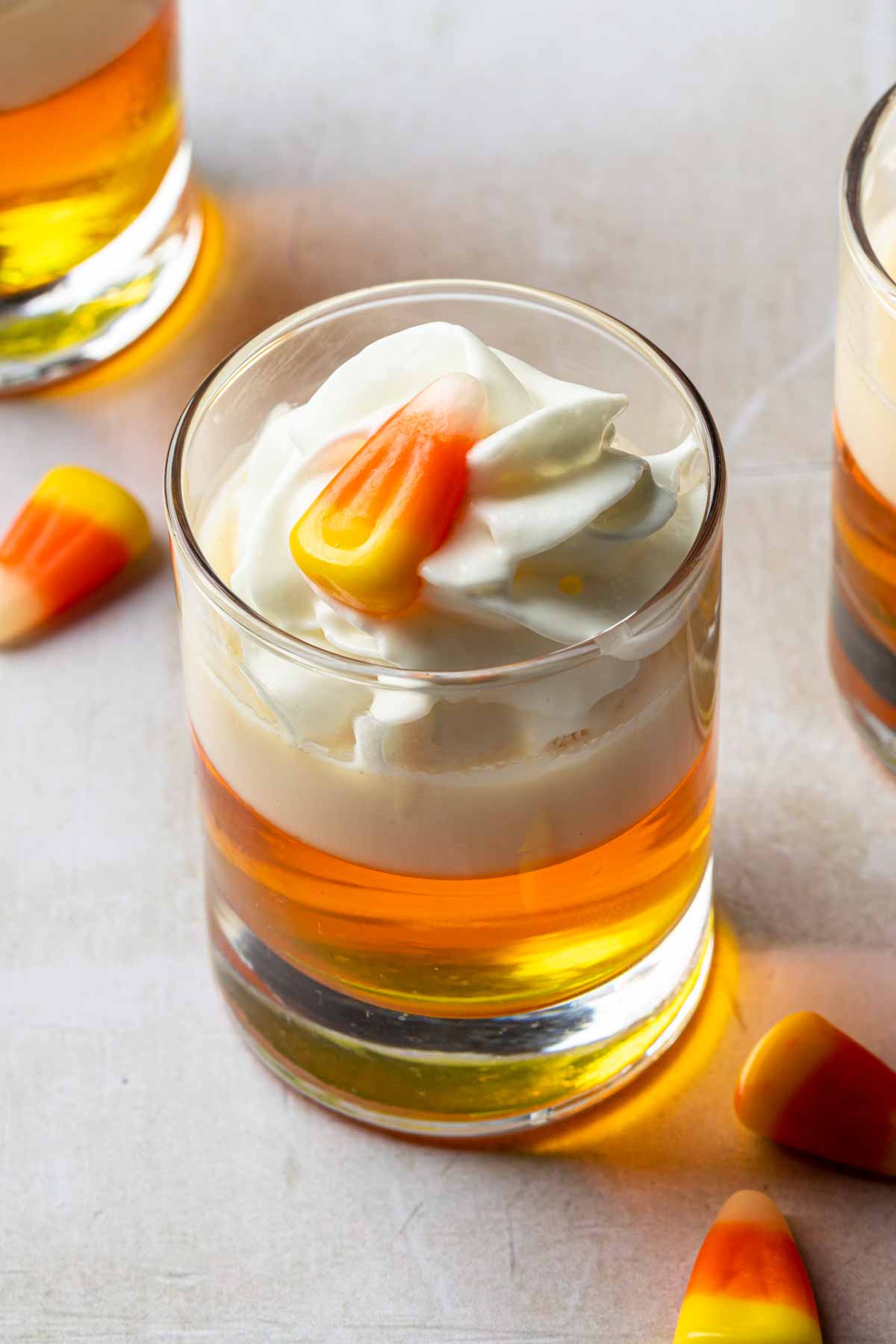 Close up of a candy corn jellow shot, garnished with whipped cream and a single piece of candy corn. 