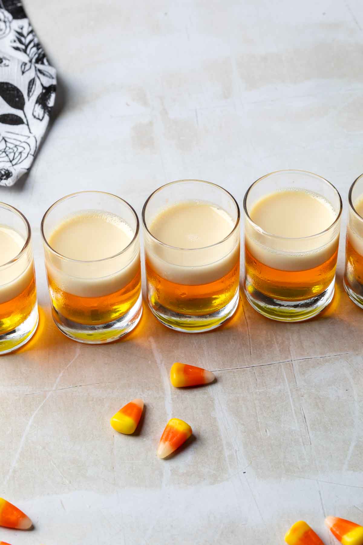 Candy corn jello shots in a line with a few candy corn pieces laying in front of them. 