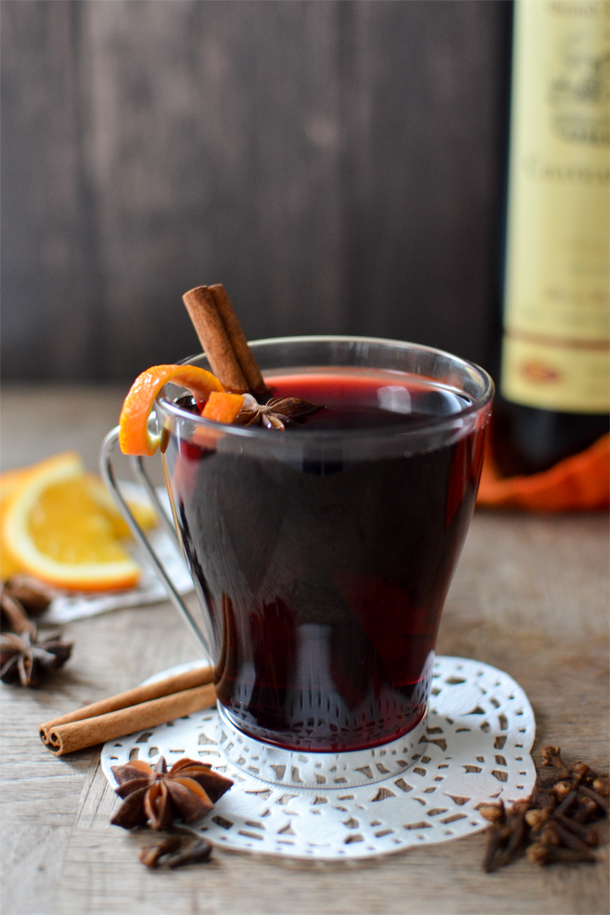 Vin chaud in a glass mug on a doily, garnished with an orange twist and a cinnamon stick. 