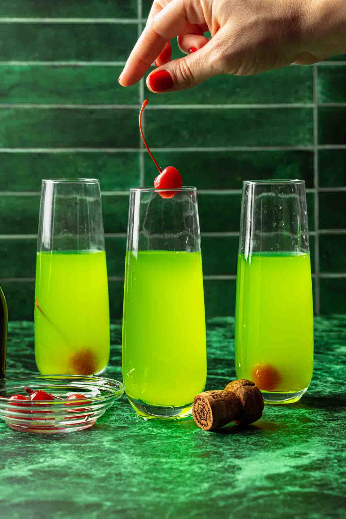 A cherry being dropped into a bright green prosecco drink. 