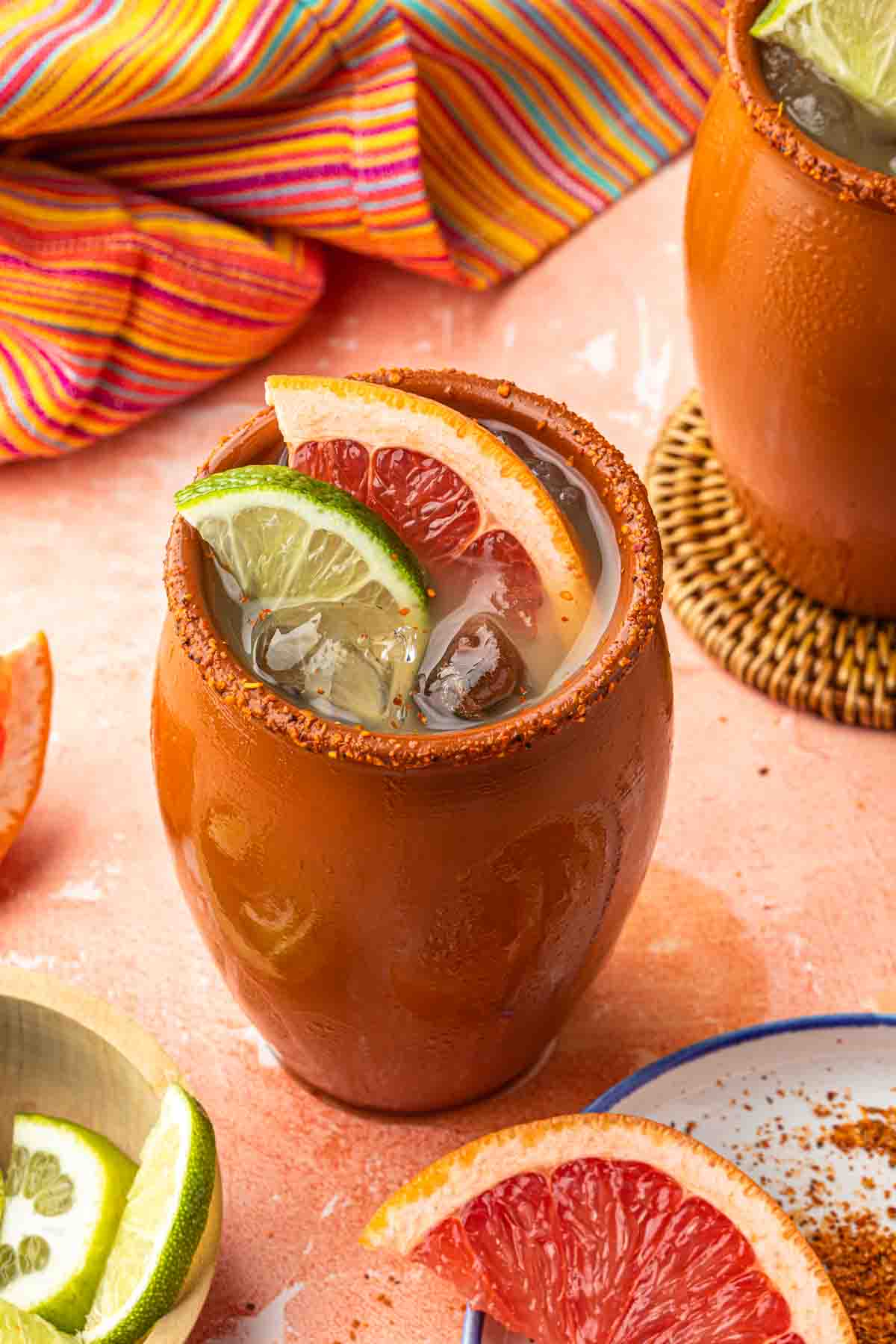 Cantaritos cocktail in a traditional clay cup, garnished with grapefruit and lime, rimmed with tajin. 
