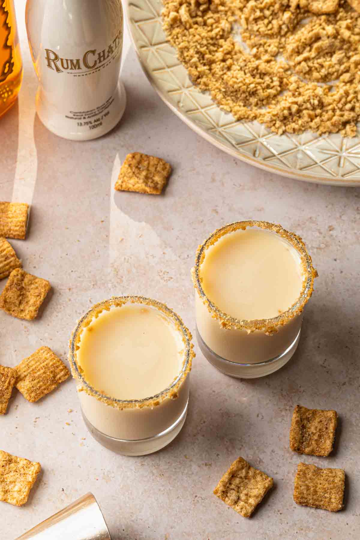 Cinnamon toast crunch shots in glasses rimmed with crushed cereal. 