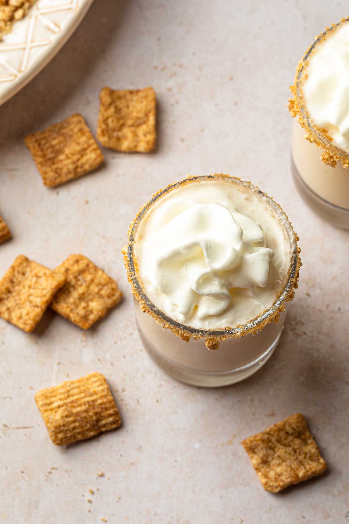 A cinnamon toast crunch shot topped with whipped cream with cereal laying around it. 