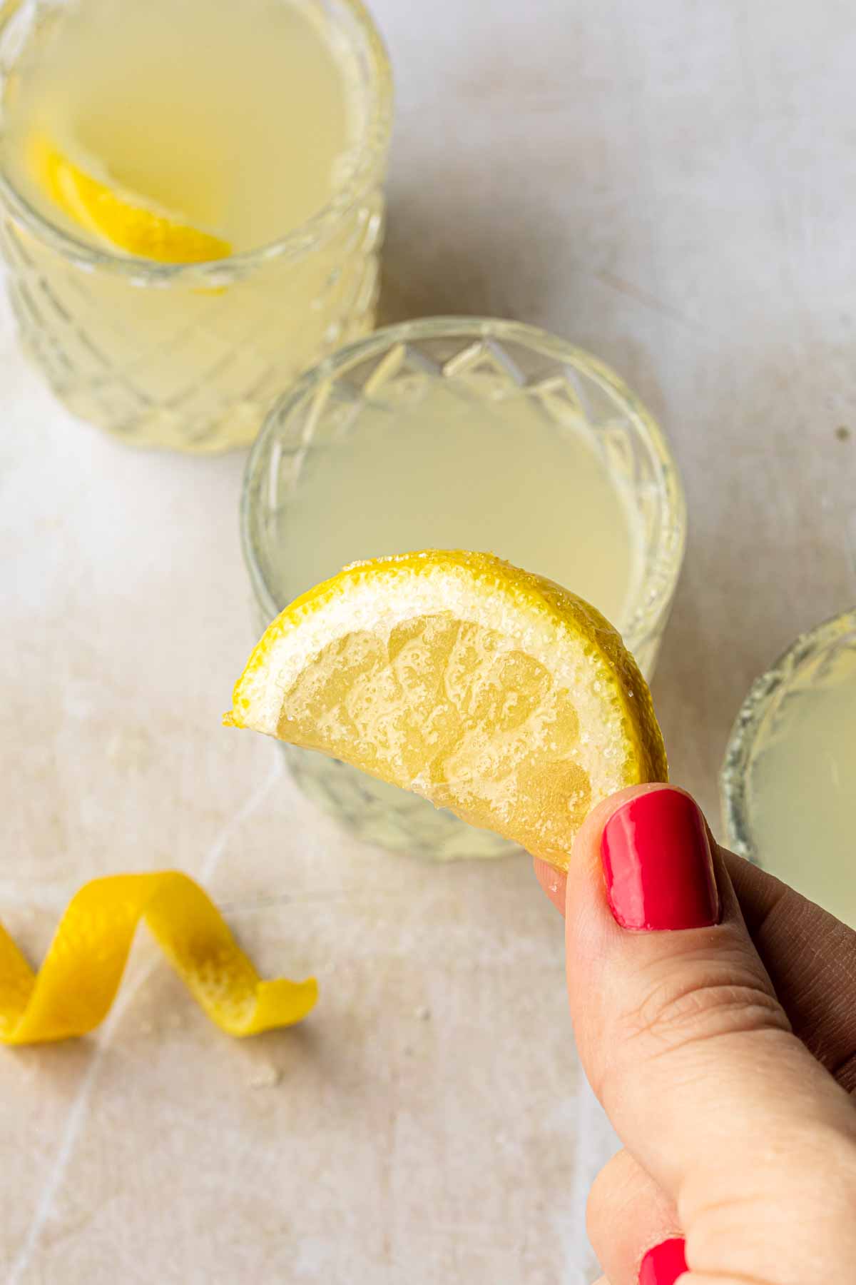 A hand holding a lemon wedge covered in sugar, above a few shot glasses. 
