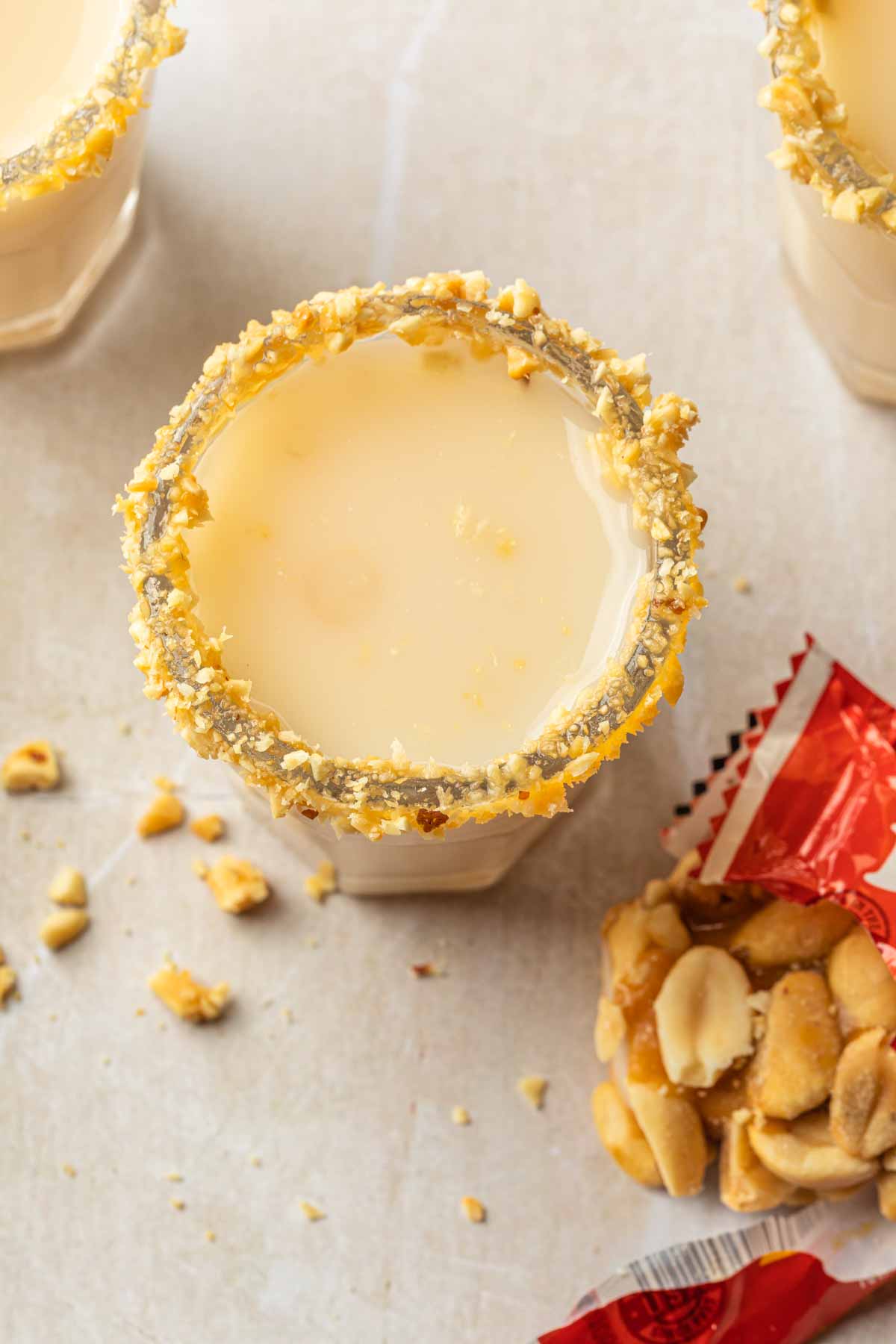 A salted nut roll shot in a shot glass rimmed with peanuts next to an open nut roll candy bar. 