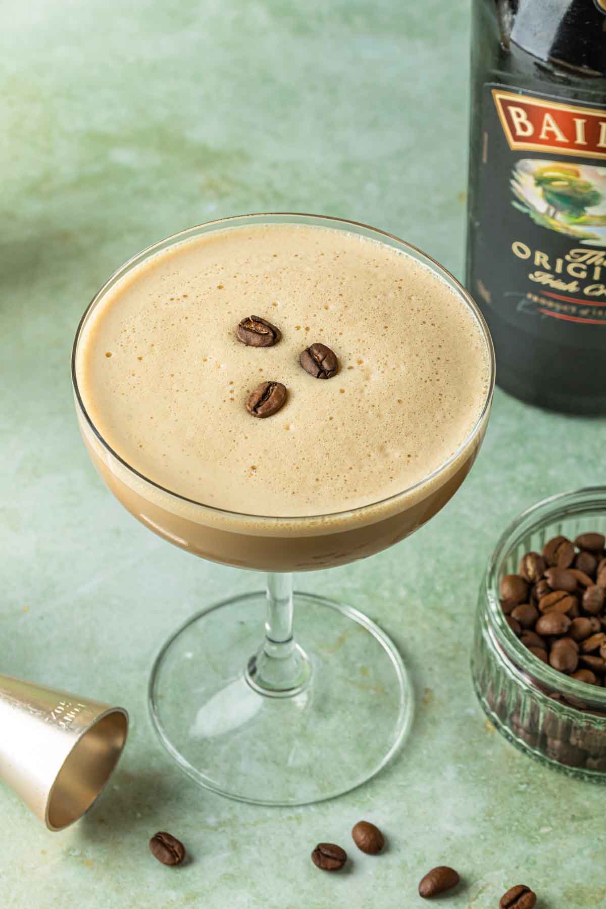 An irish cream and coffee liqueur martini with espresso beans floating on the frothy top. 
