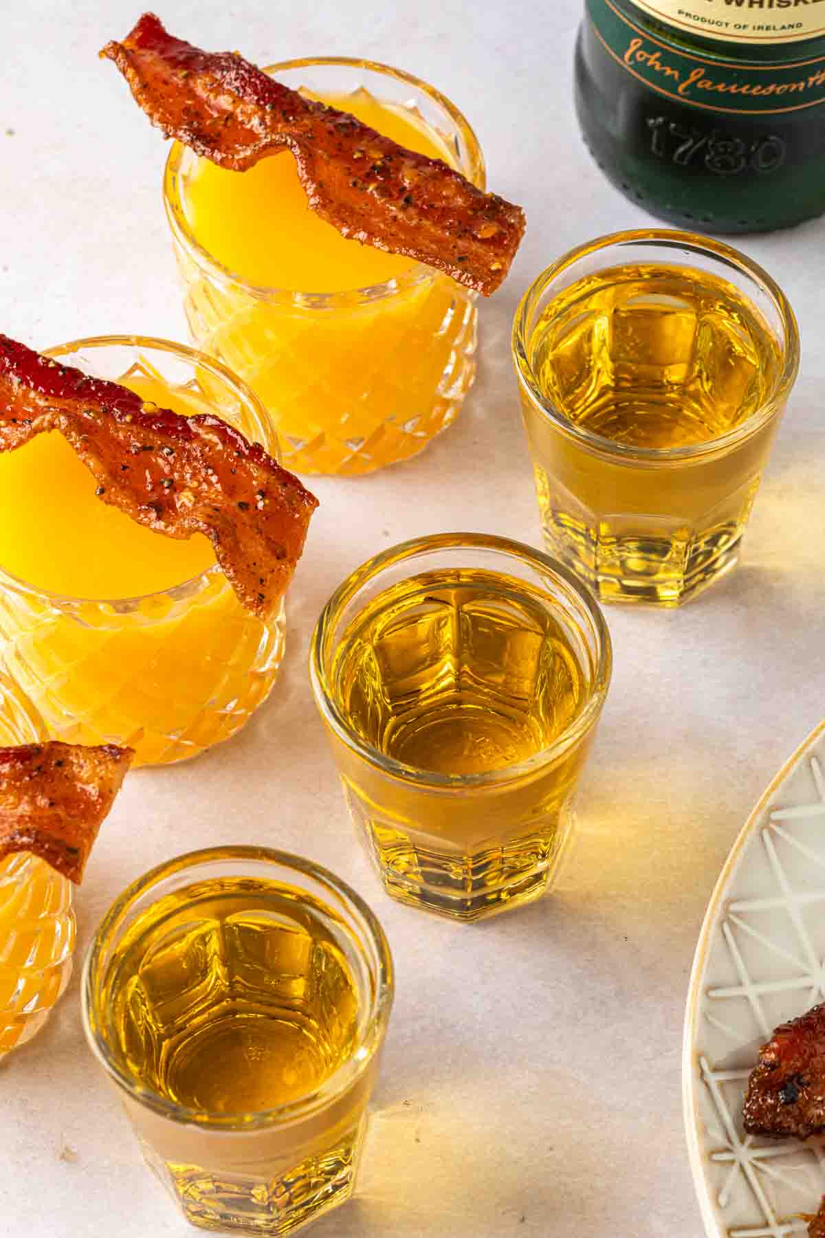 3 Irish breakfast shots in a line, next to a bottle of Jameson and a plate of bacon. 