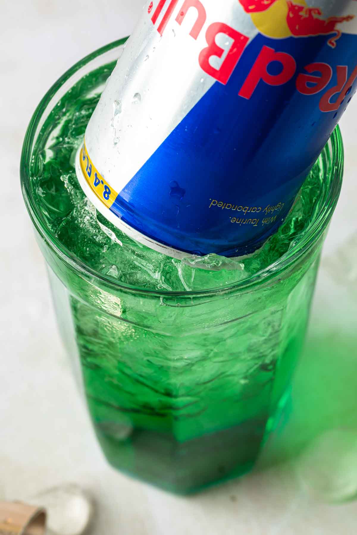 Close up of a red bull tipped into a tall green cocktail. 