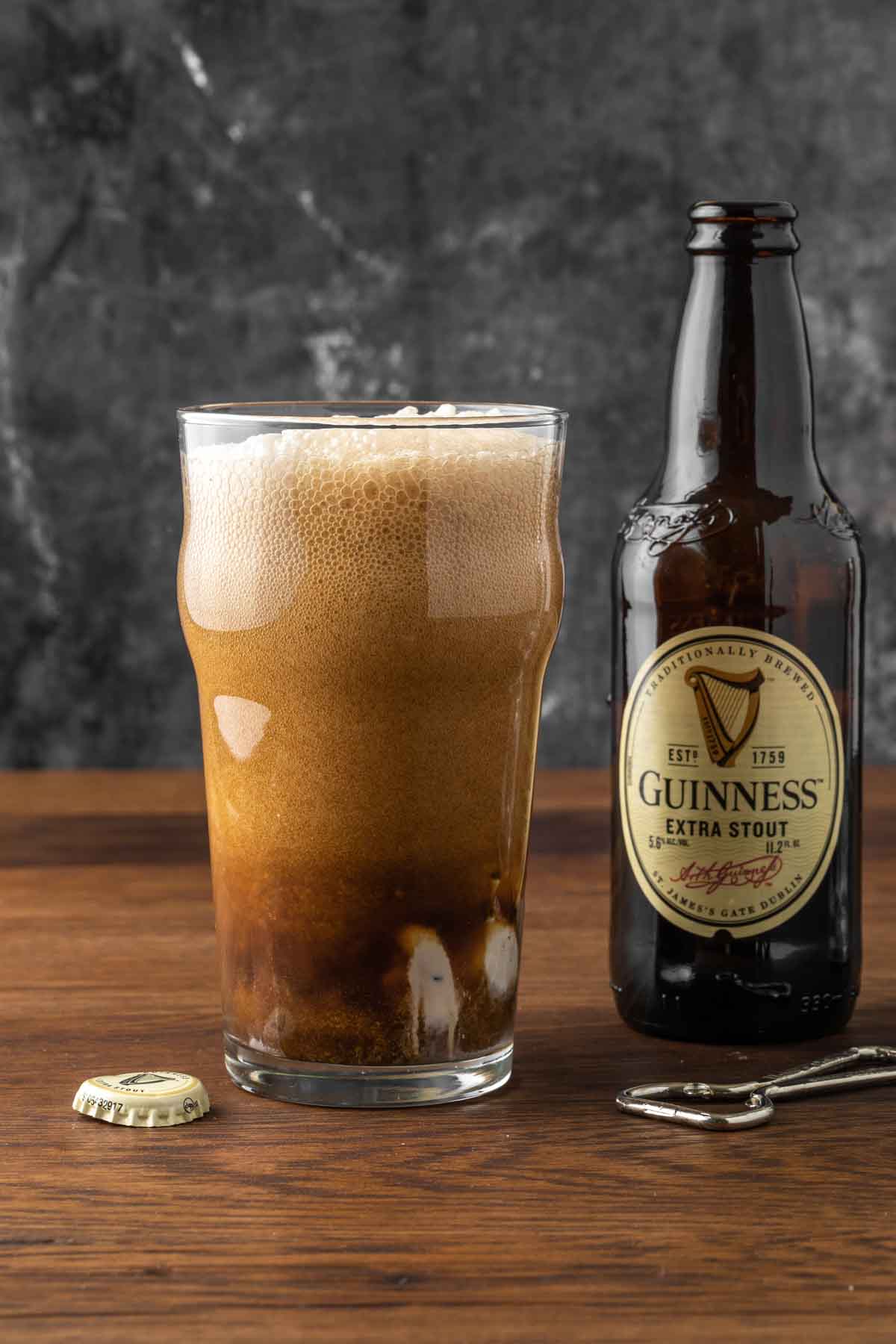 A guinness beer float in a glass next to a bottle of guinness. 