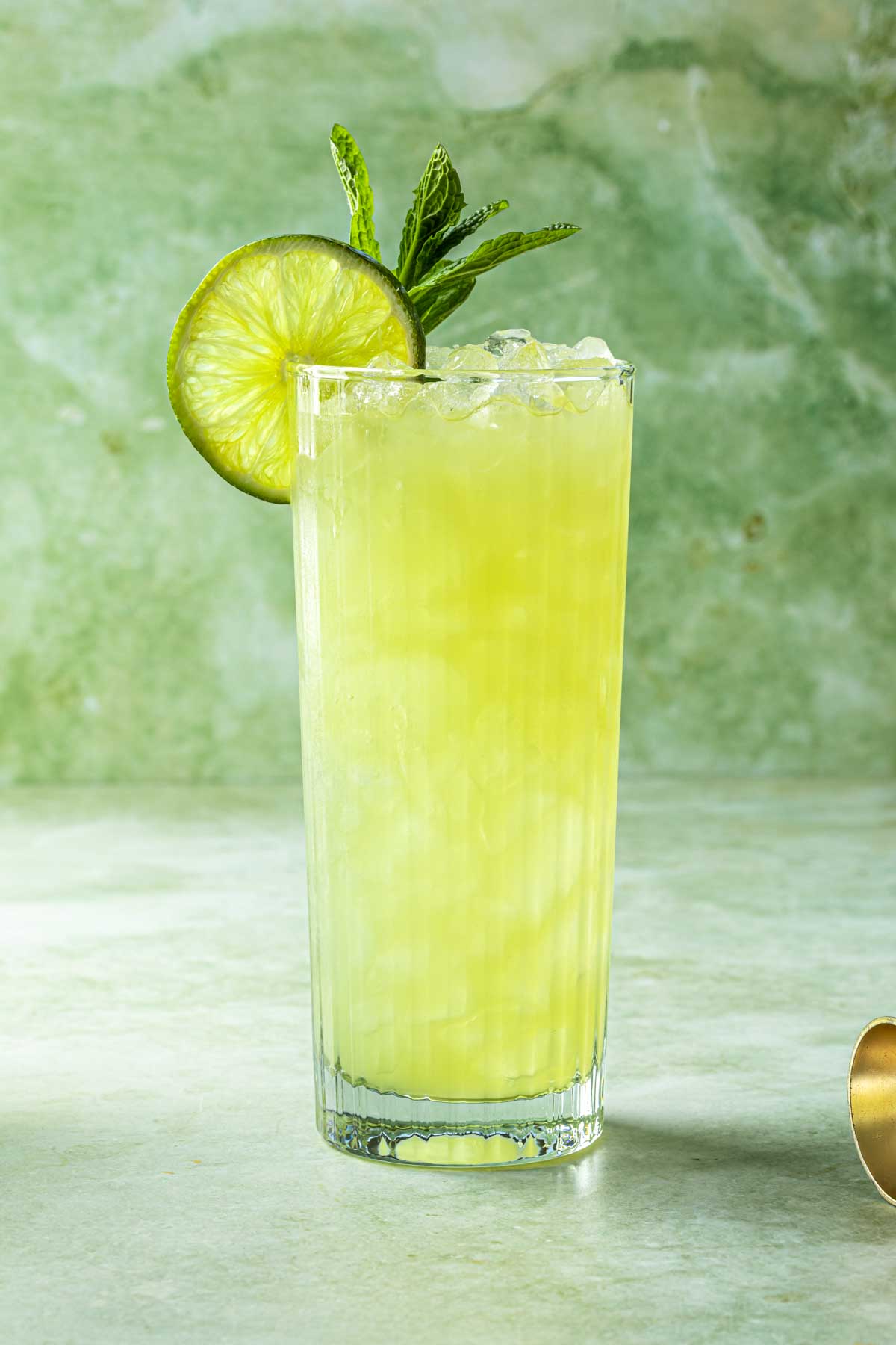 A chartreuse swizzle cocktail in a tom collins glass, garnished with a lime wheel and fresh mint. 