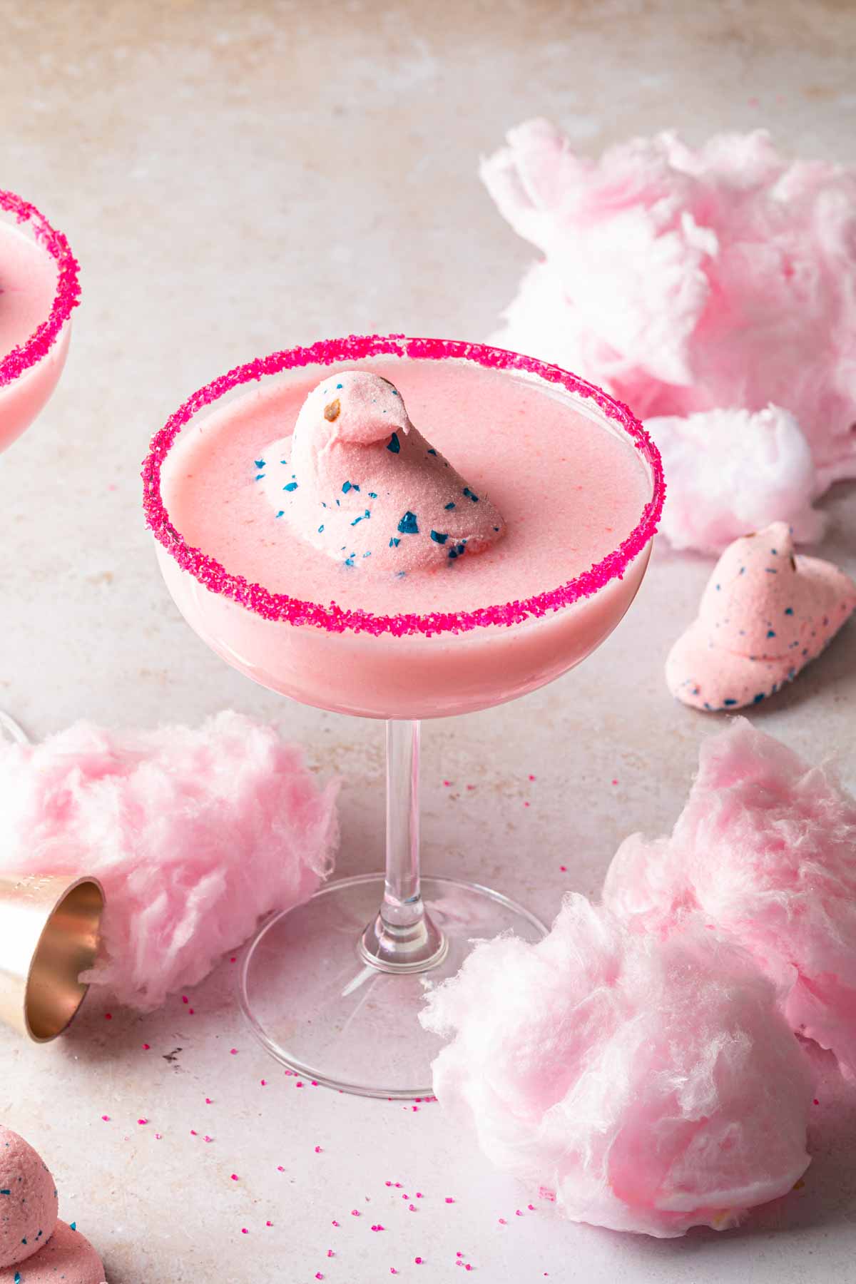 A couple of pink cotton candy martinis surrounded by cotton candy and easter peeps. 