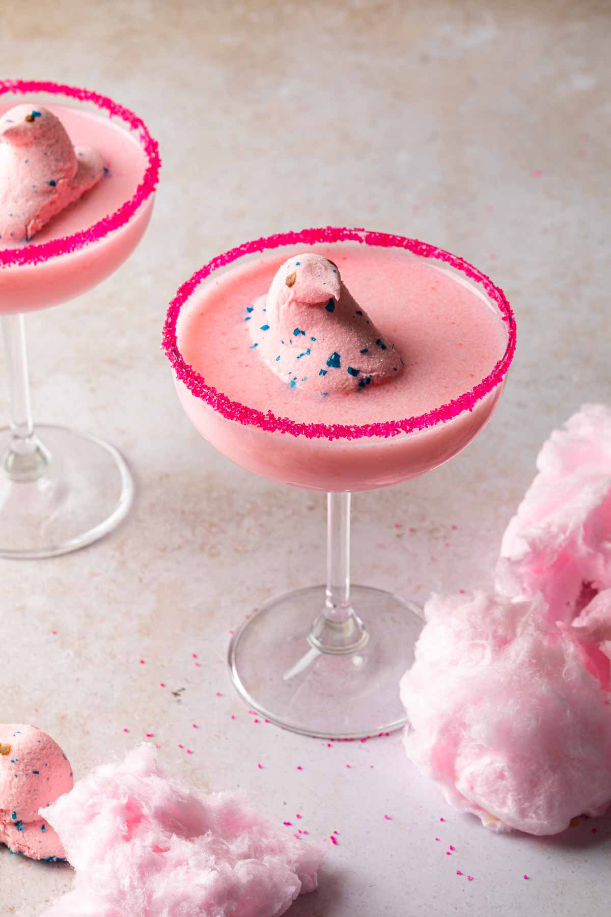 A couple cotton candy cocktails surrounded by cotton candy, garnished with easter peeps. 