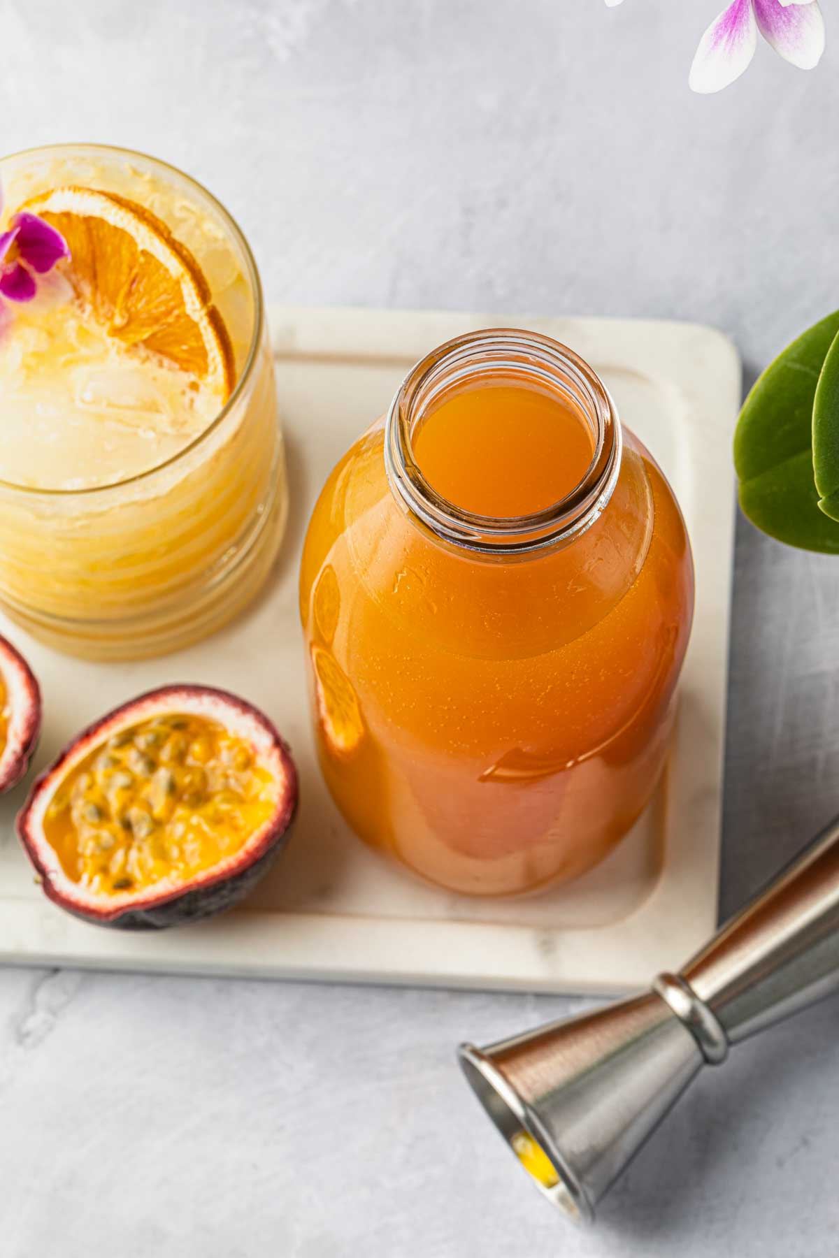 A bottle of passion fruit cocktail syrup next to a cocktail and a passion fruit. 