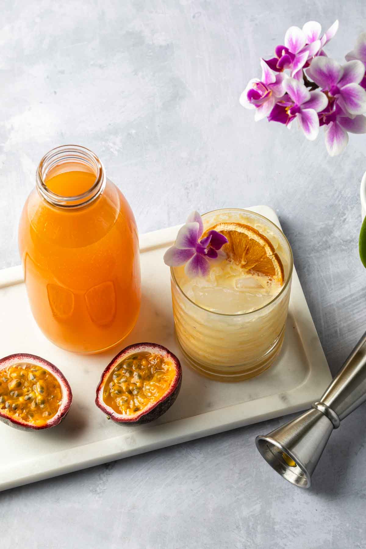 A cocktail and a bottle of passion fruit syrup on a serving tray with a passion fruit cut open. 