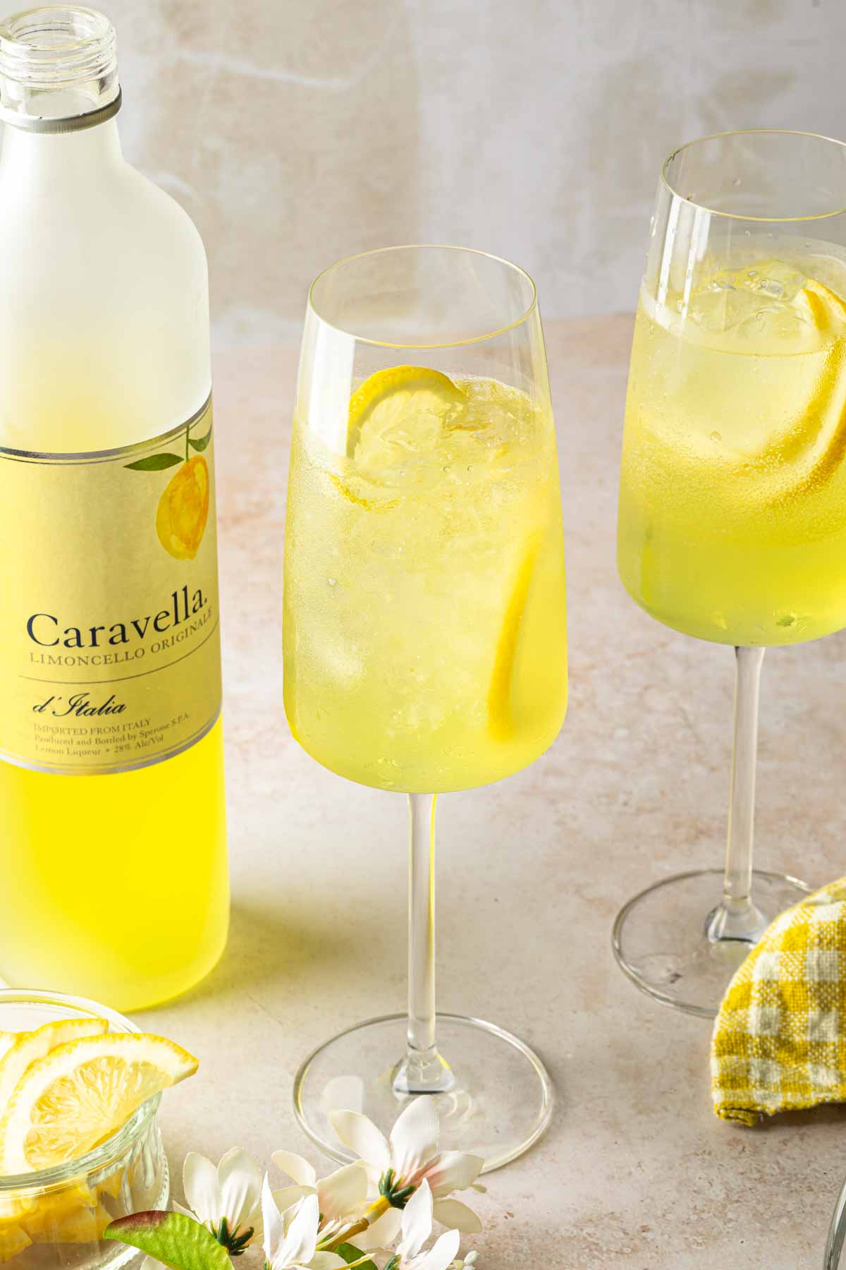 A couple of limoncello spritz cocktails in tall wine glasses, next to a bottle of limoncello. 
