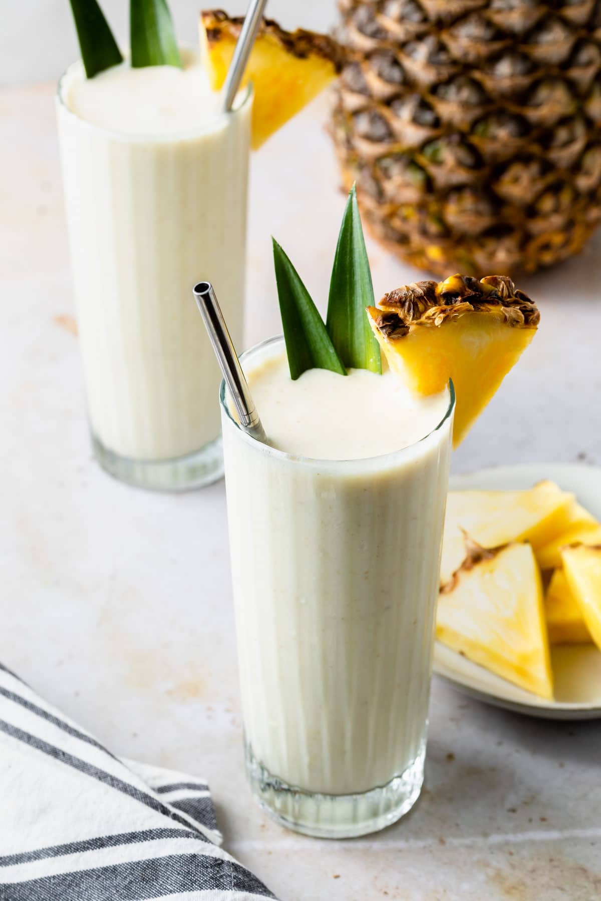 Pineapple coconut yogurt smoothies in tall glasses in front of a pineapple. 