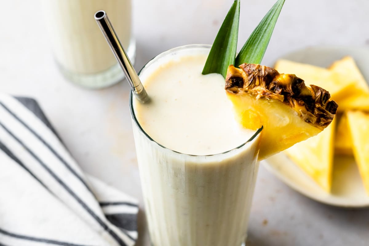 A pineapple coconut smoothie in a glass with a plate of pineapple wedges in the background. 