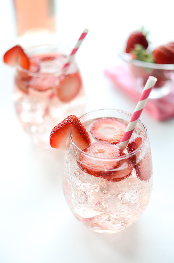 A couple glasses of a sparkling wine sangria, with pink straws and a bowl of strawberries. 