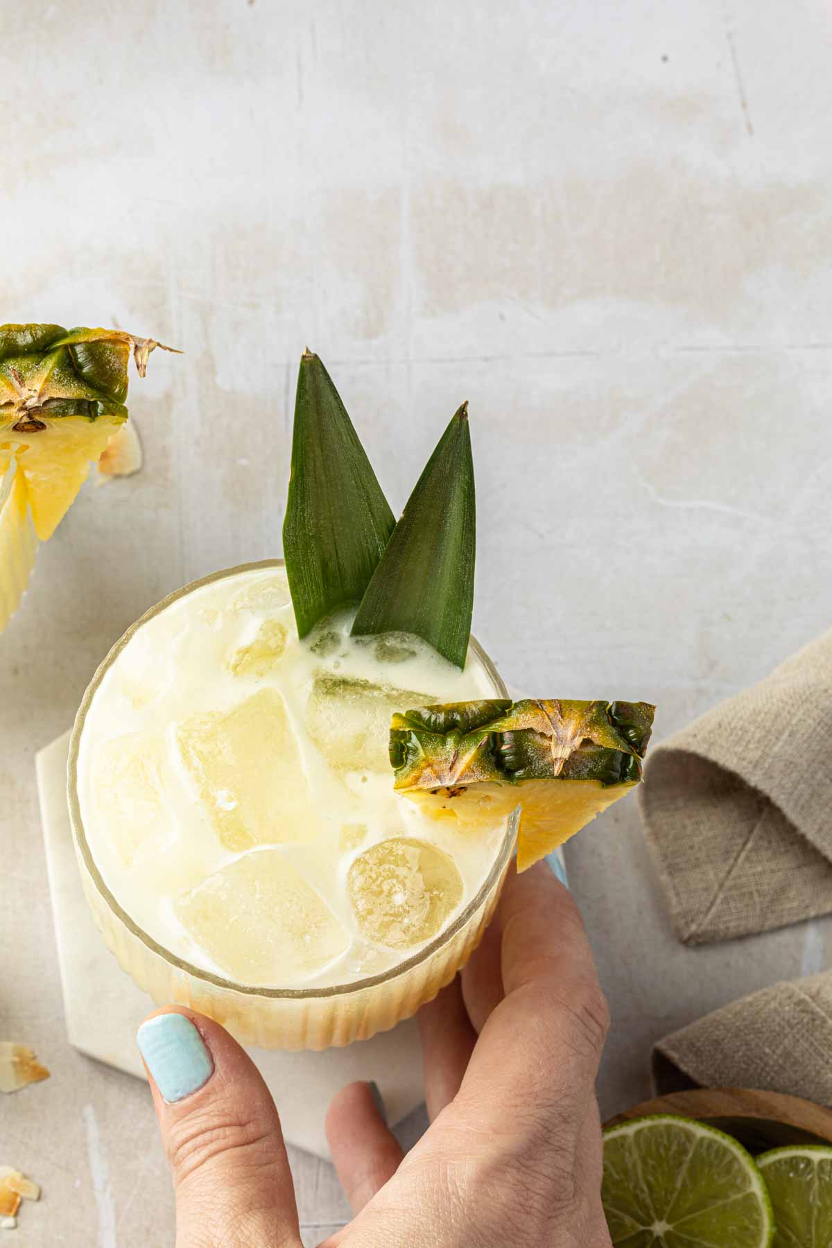 A hand picking up a cocktail garnished with pineapple. 