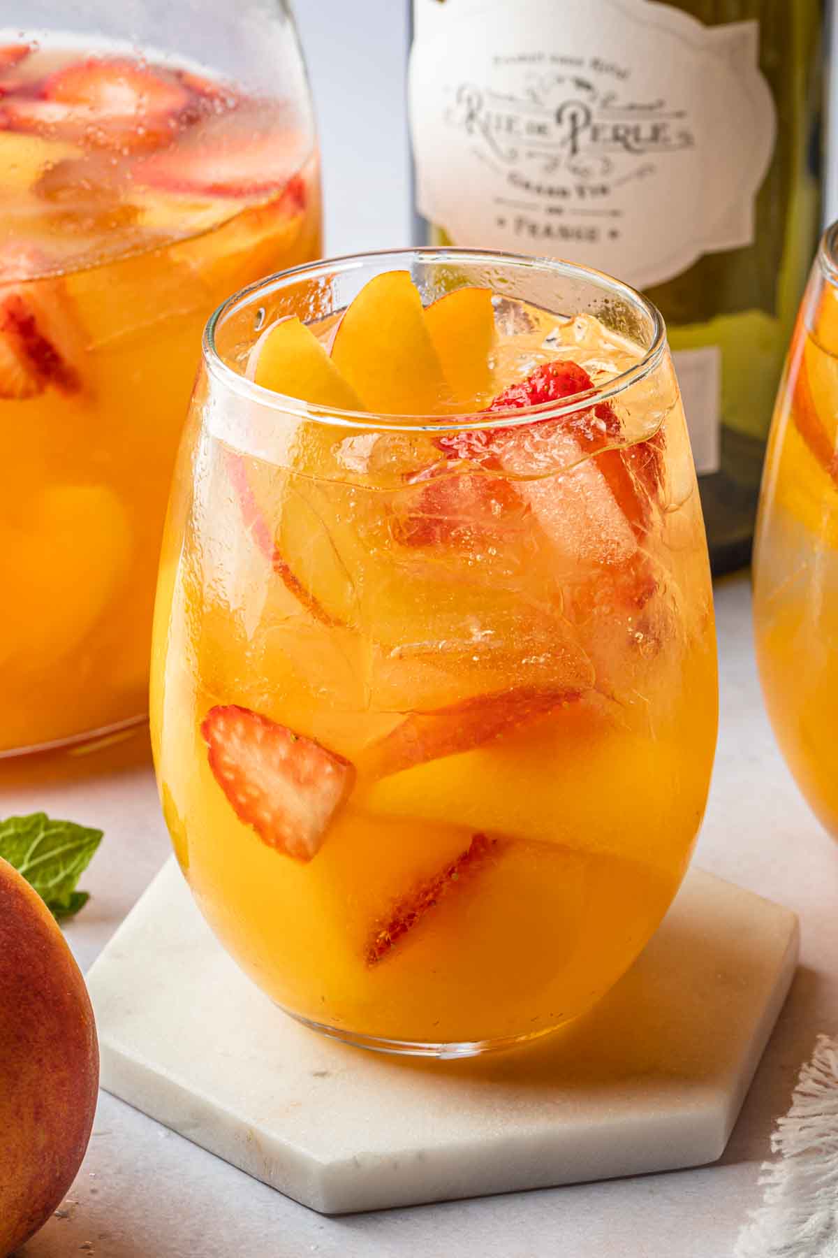 Close up of a wine cocktail with strawberries and sliced peaches floating in the glass. 