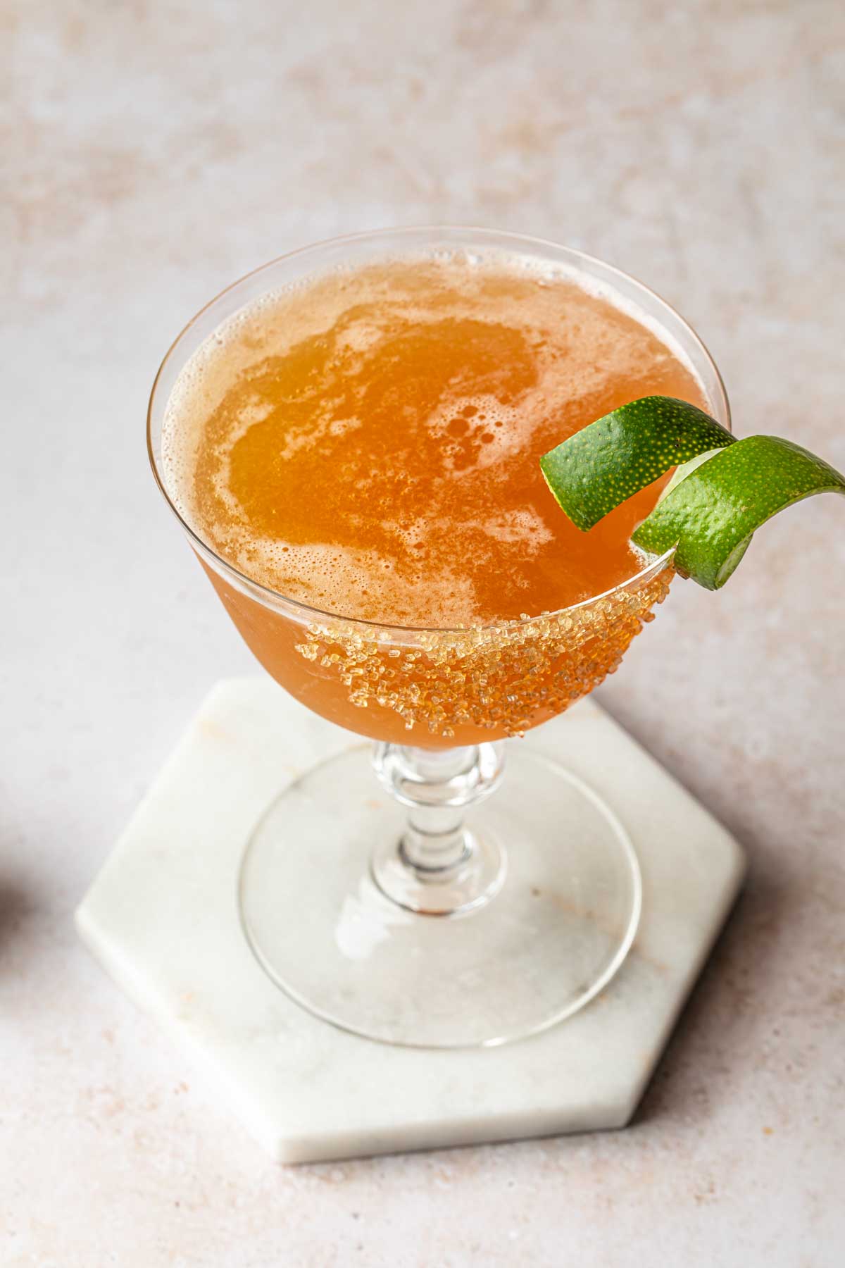 A lion's tail cocktail in a vintage coupe glass, rimmed with raw sugar and garnished with a lime twist. 