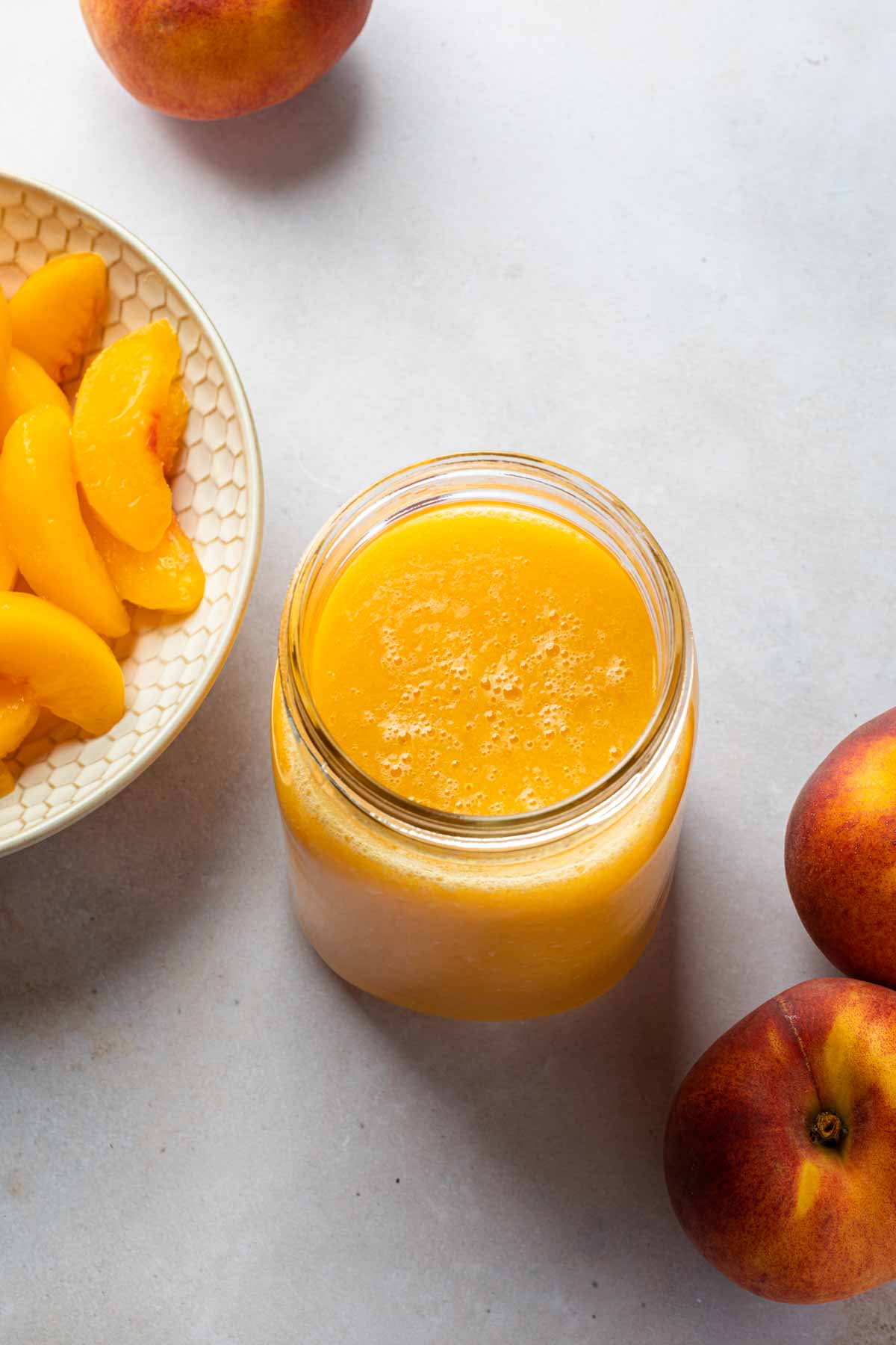 A mason jar full of a thick puree of fruit next a bowl of peaches. 