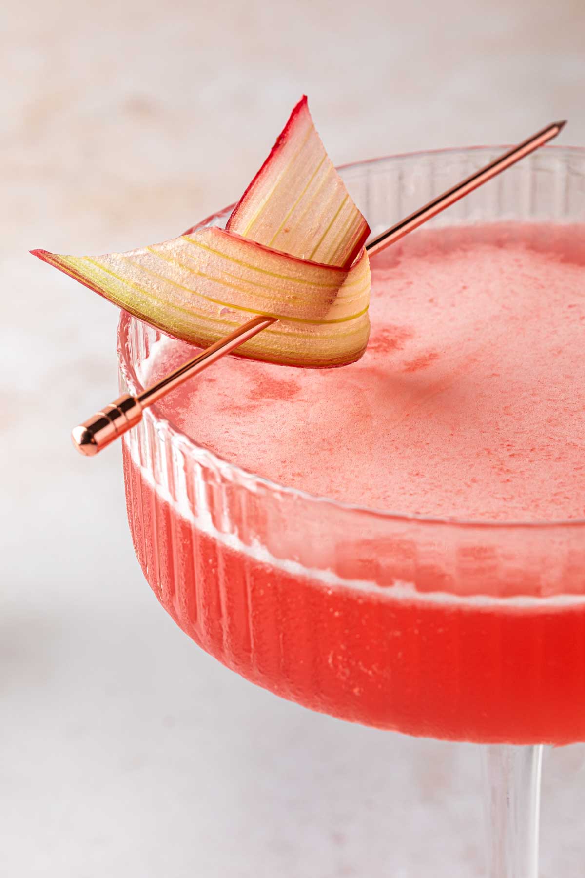 Close up of a rhubarb twist resting on a cocktail in a coupe glass. 