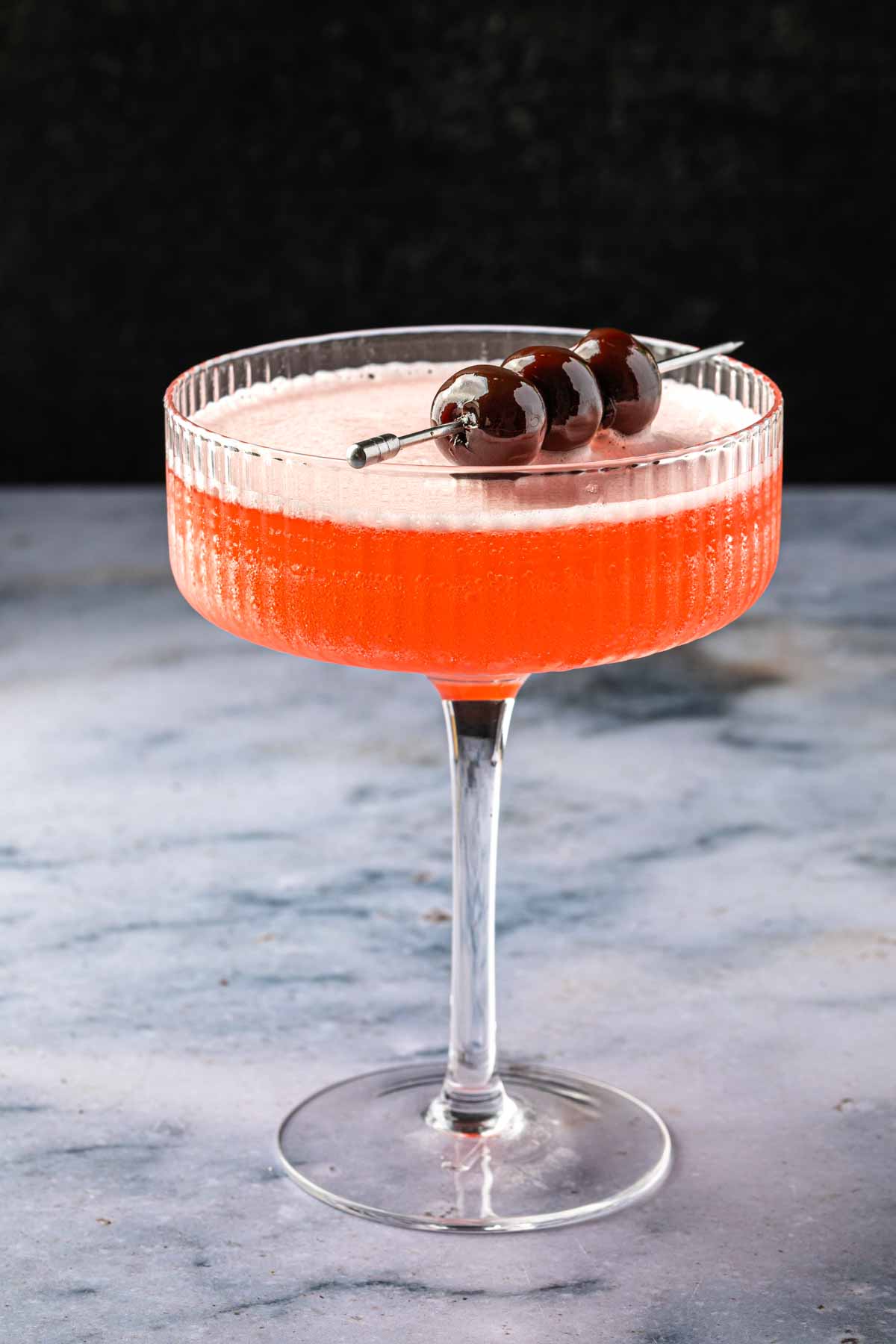 A coupe glass with a mary pickford cocktail, garnished with cocktail cherries. 
